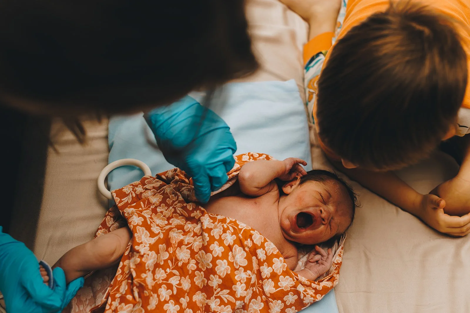 Newborn baby crying on delivery bed, surrounded by medical staff and parents.