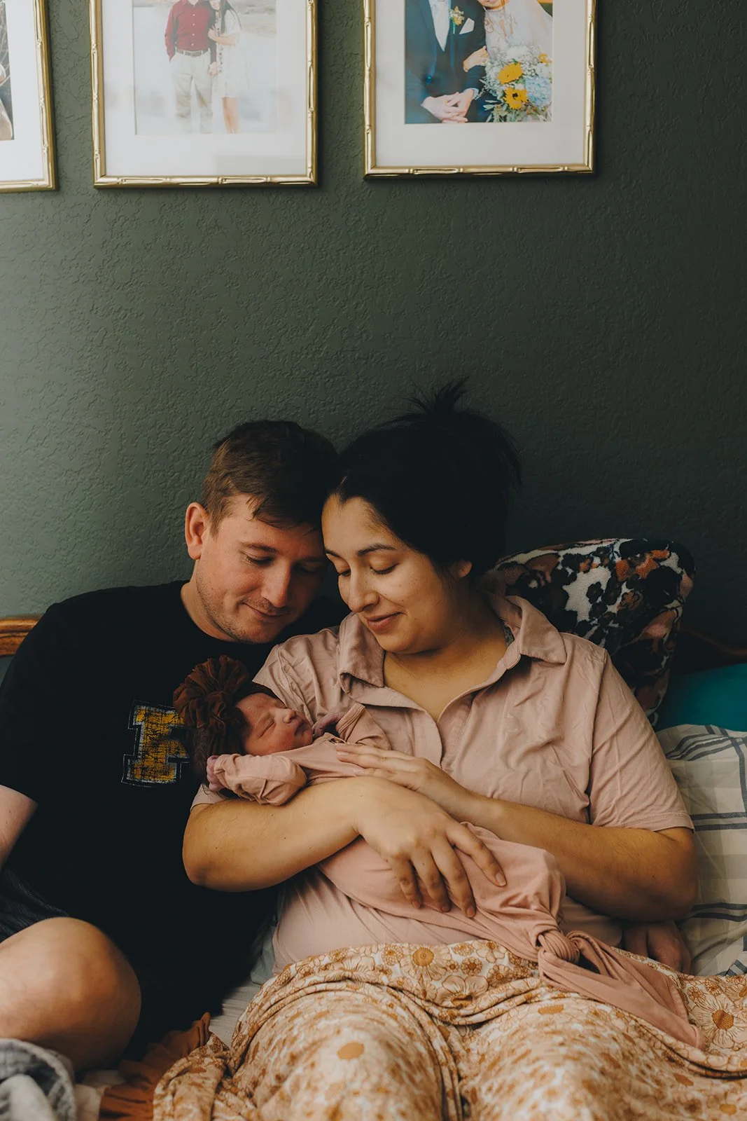 A father and mother cradle their newborn baby while resting in bed. 