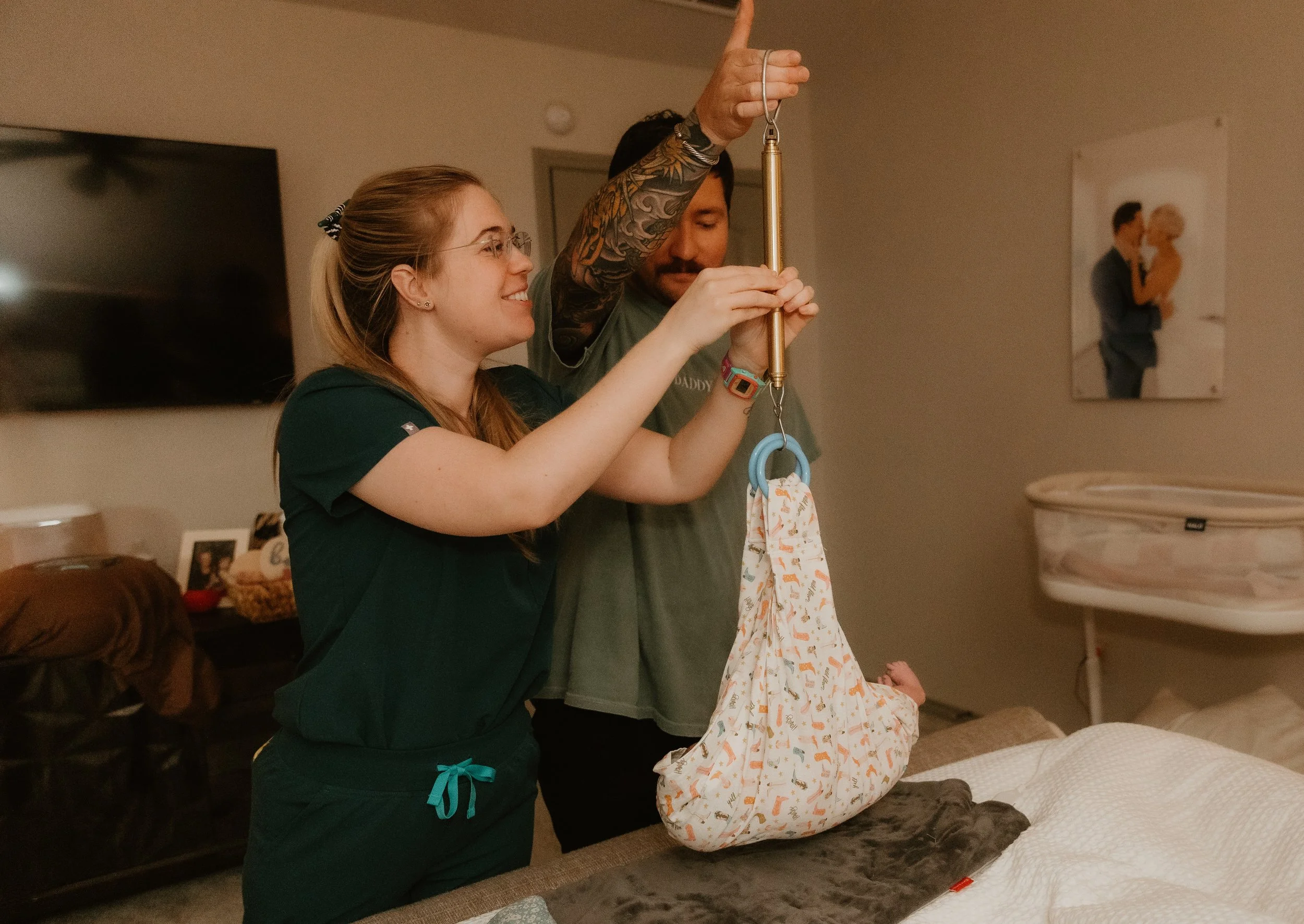 A midwife and dad weigh a newborn baby post home birth.