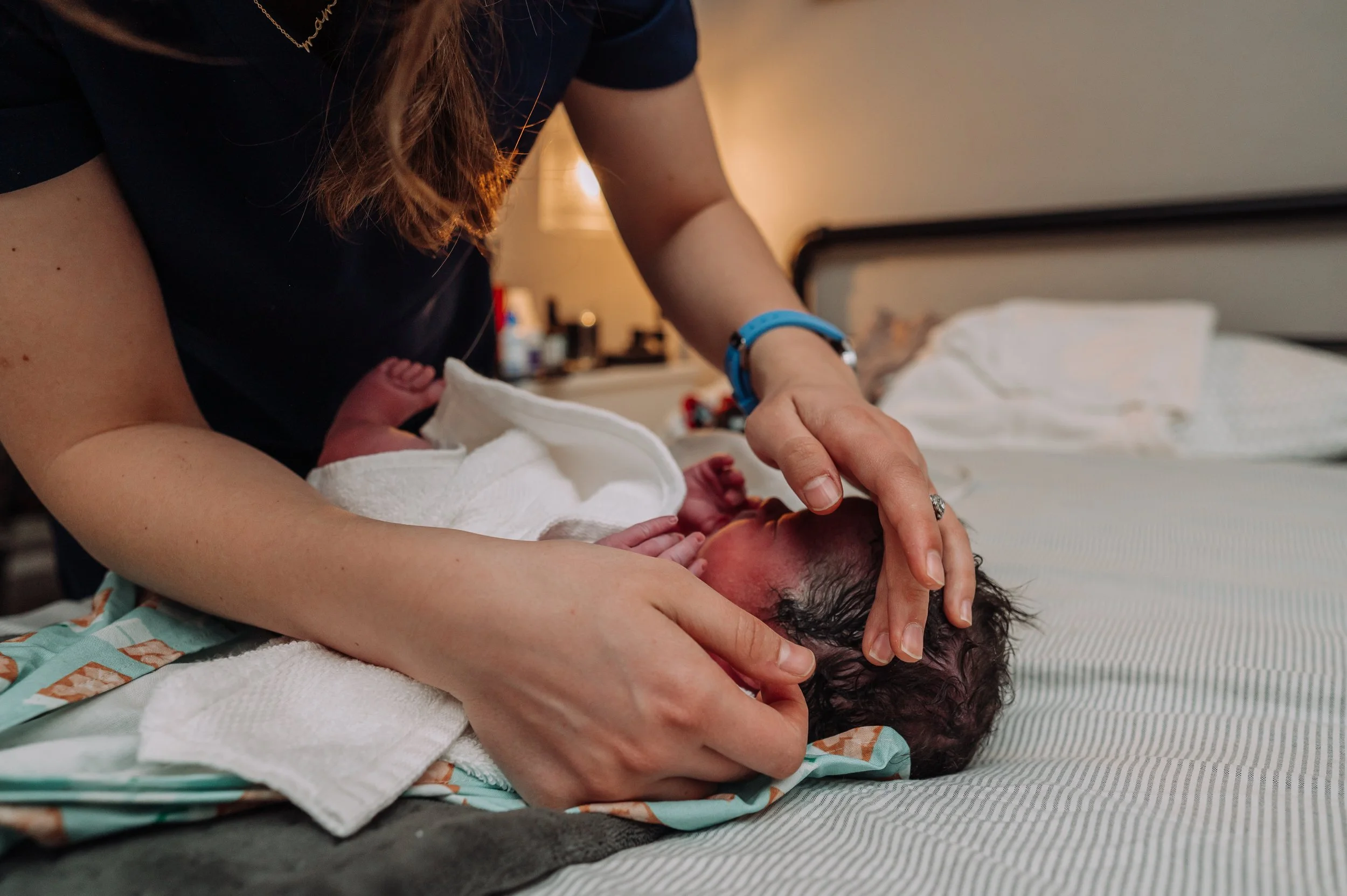 A midwife completes a head to toe newborn assessment on the bed next to mom and dad.