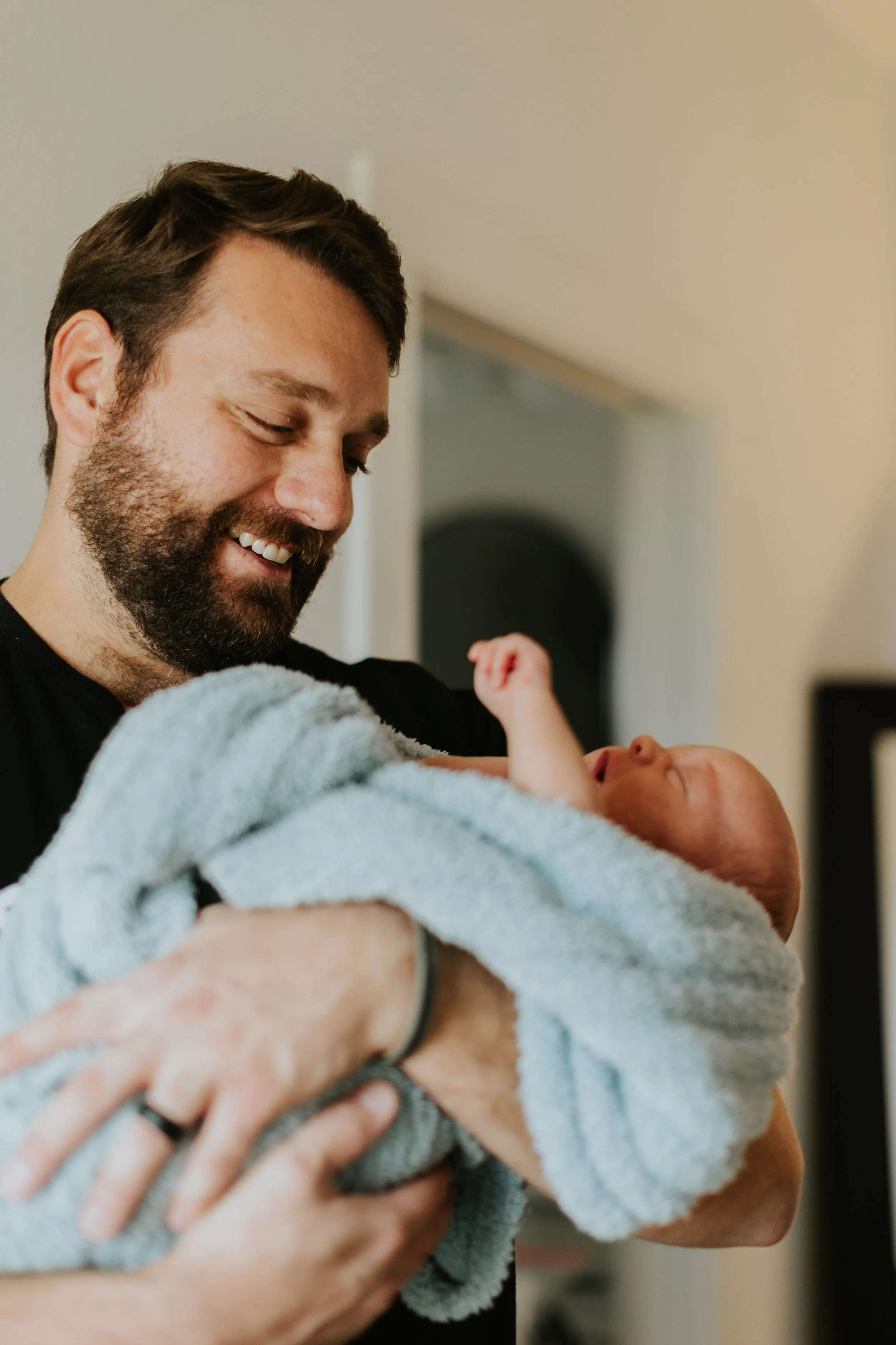 A father holds his newborn in a fluffy blanket while smiling.