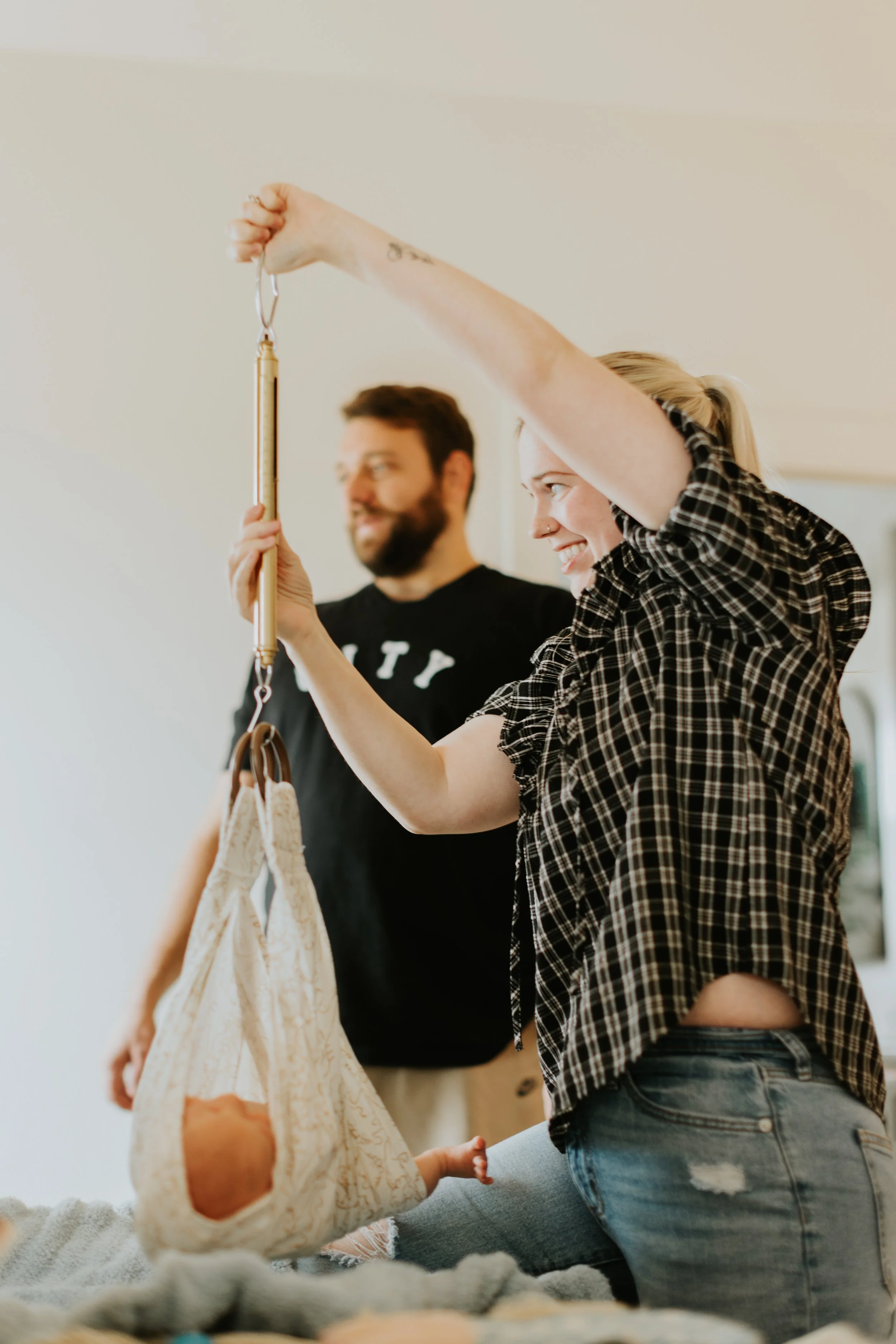 A home birth midwife and father weigh a newborn baby at a routine home visit.