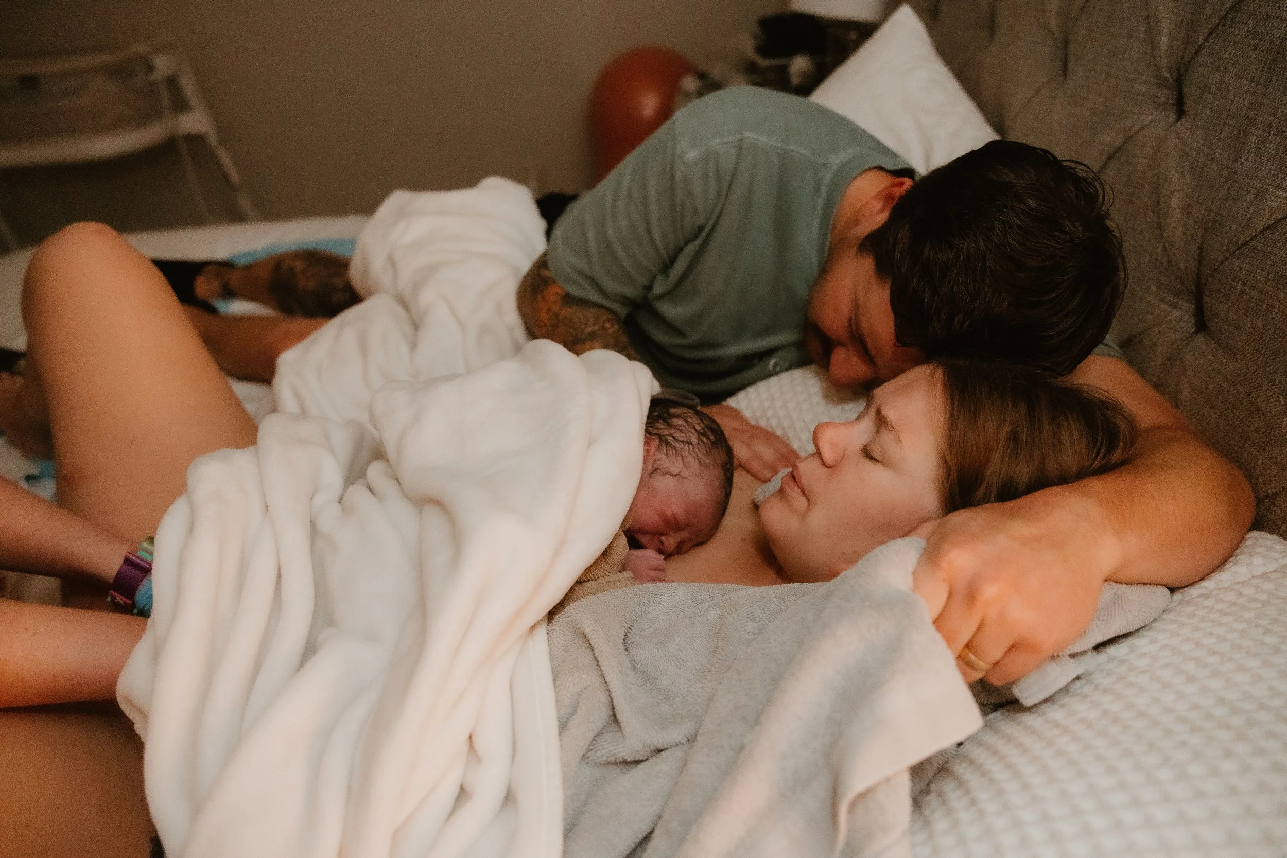 A father hugs his wife and baby in bed following their home birth in Lubbock Texas.