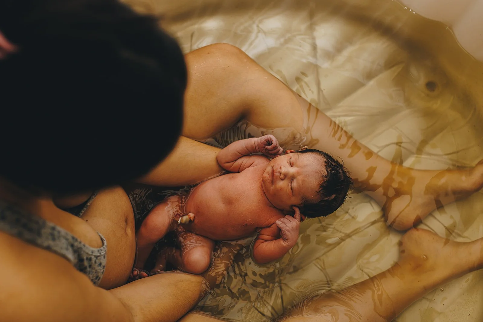 Newborn baby being born underwater, held by the mother during waterbirth.