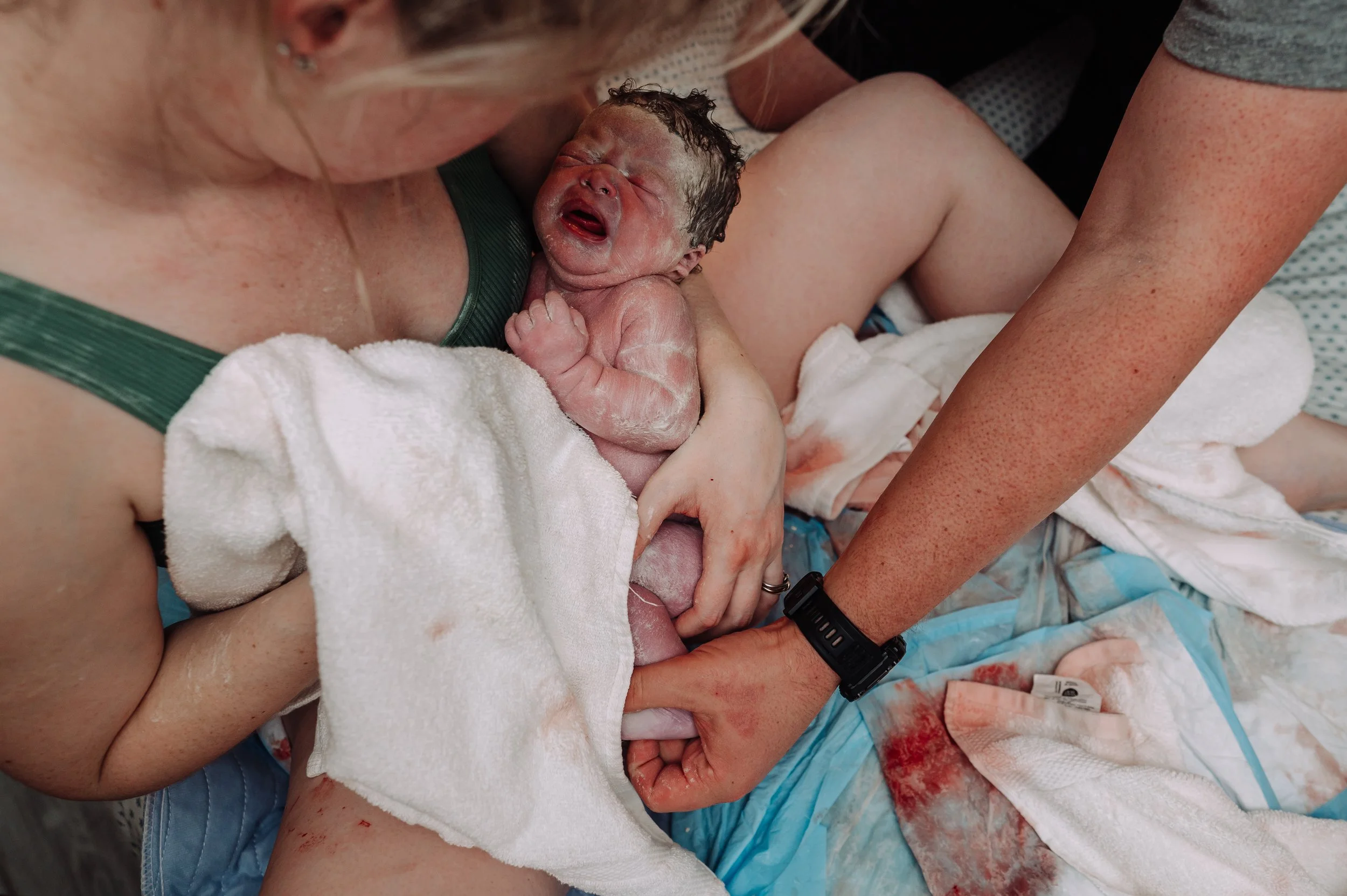 Newborn baby immediately born at home cries in mom's arms while skin to skin as the dad stimulates the baby to cry.