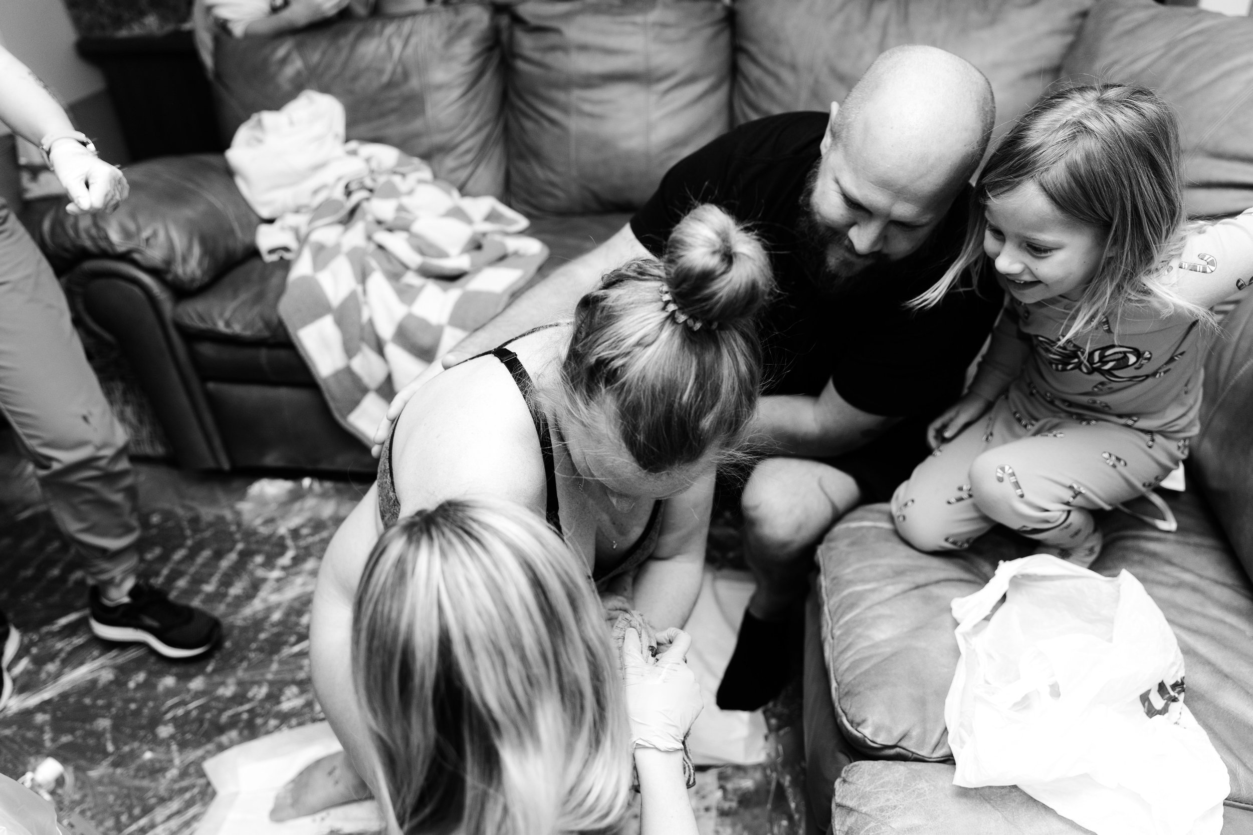 A husband and father lean in with his daughter to look at his newborn son who is being held by his mother.