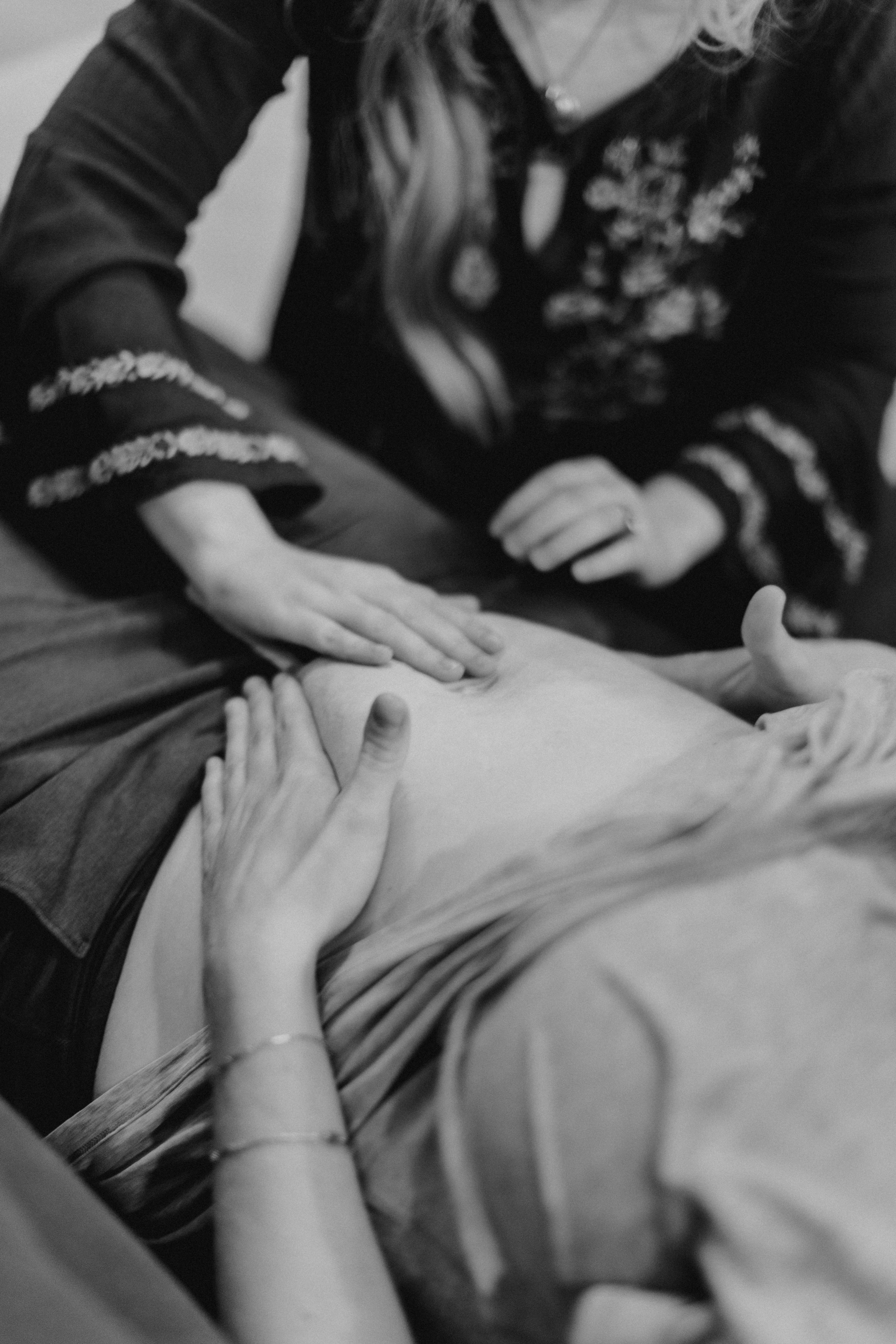 A person receiving a massage on their abdomen, with another person providing the massage, in a black-and-white photo.