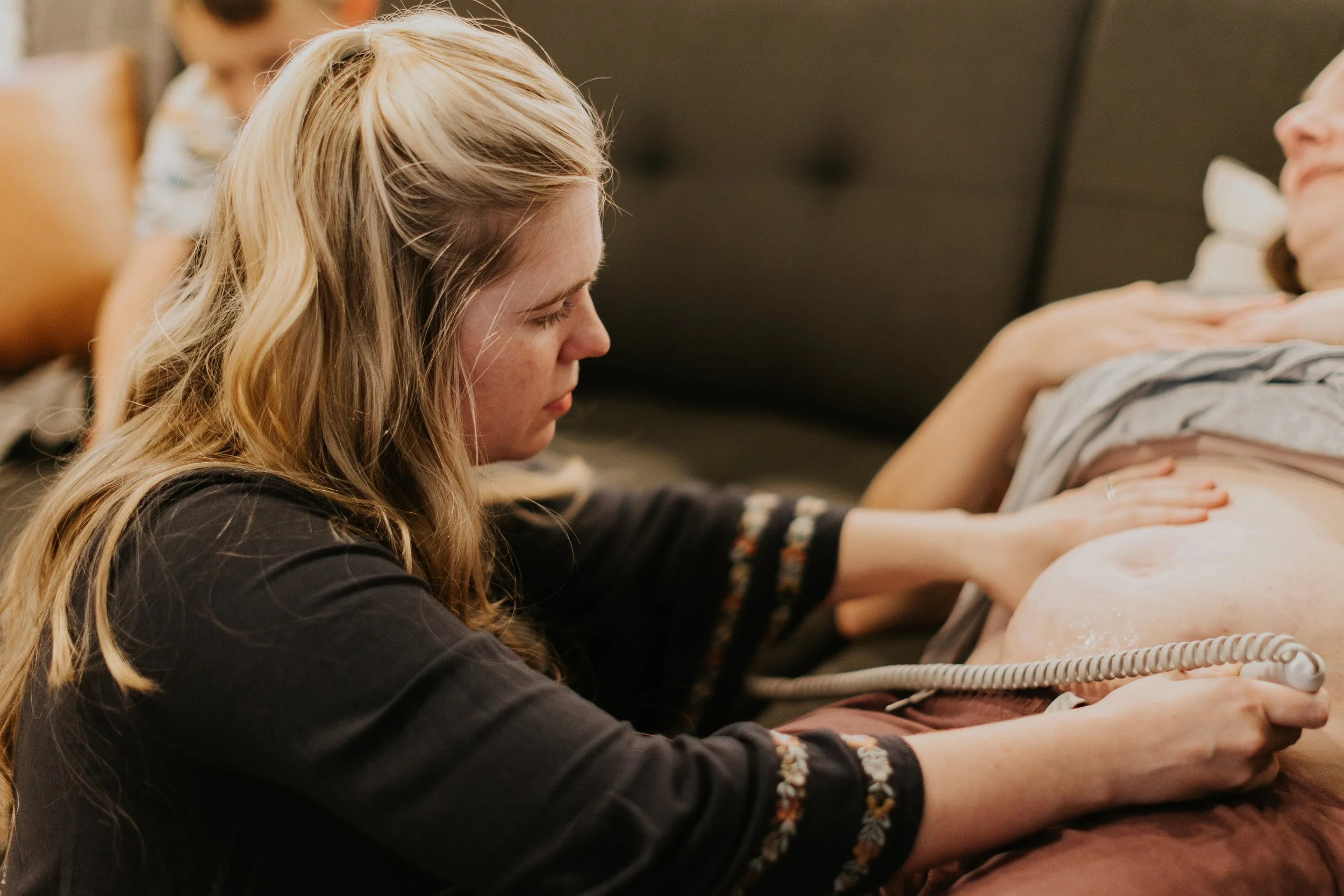A woman performs CPR on a woman lying on a bed.