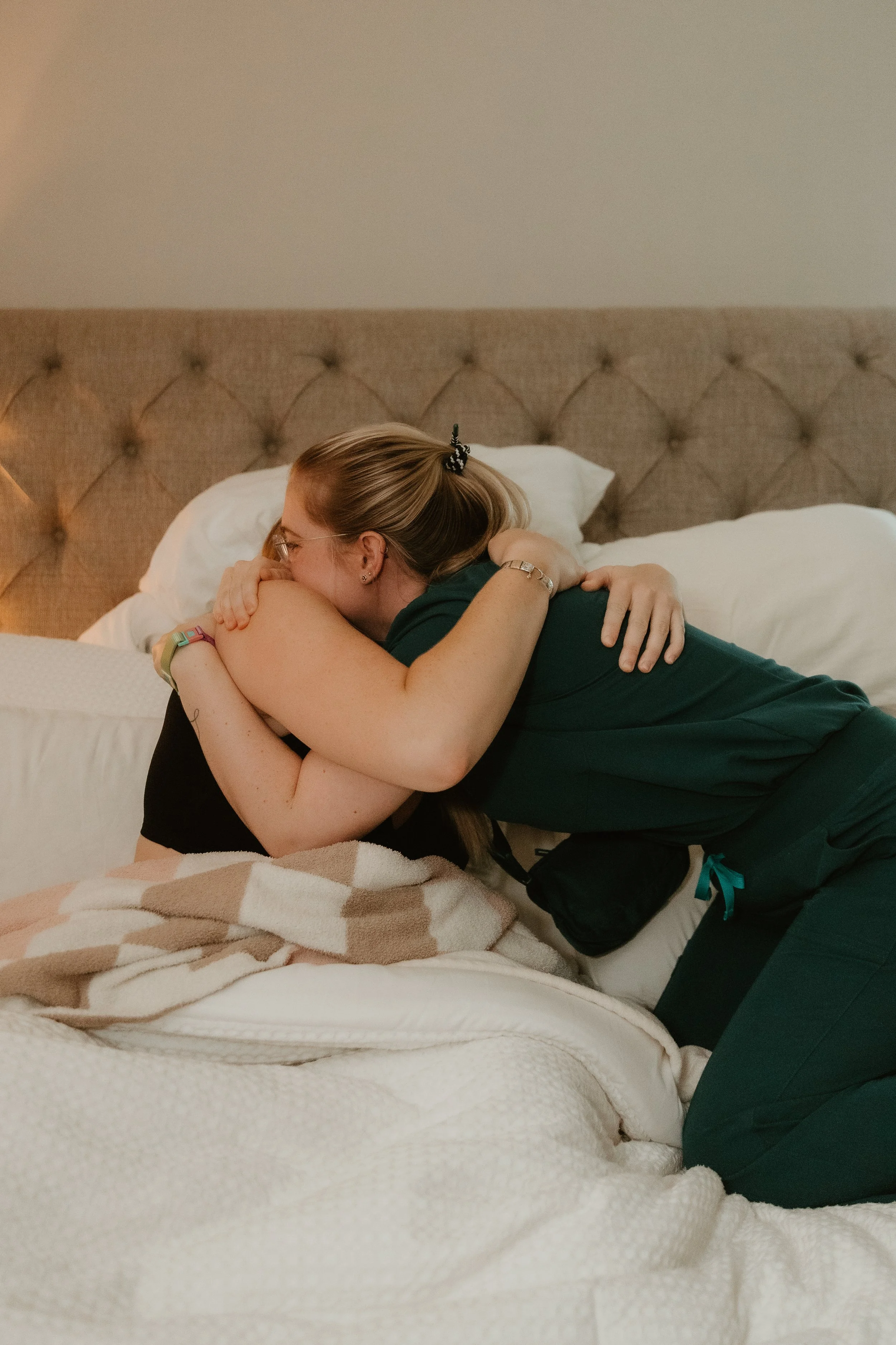 A midwife and client hug in a plush bed following birth. 