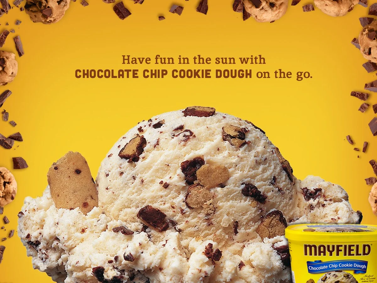 A tub of Mayfield chocolate chip cookie dough with a large scoop of cookie dough topped with chocolate chips and cookie pieces, surrounded by scattered cookie dough and chocolate pieces on a yellow background with the text encouraging fun in the sun with chocolate chip cookie dough.