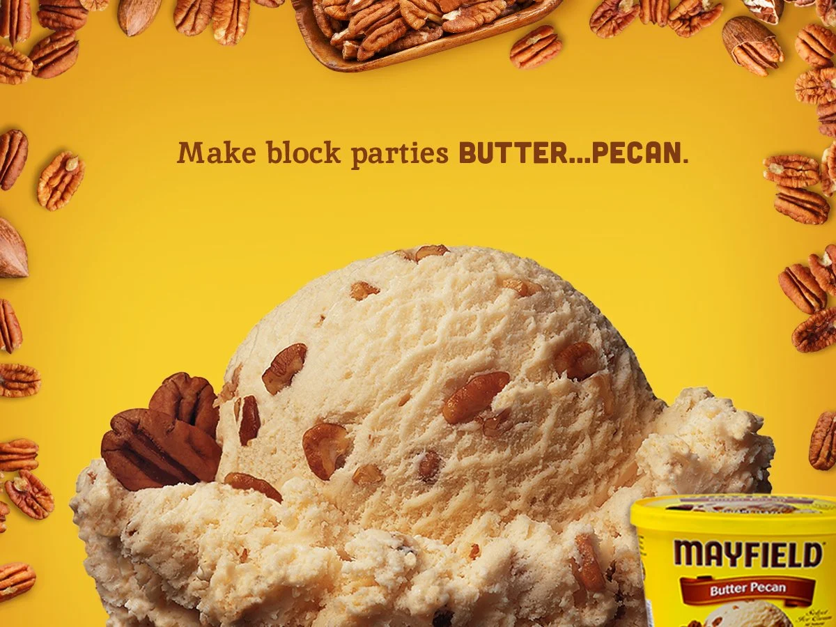 A scoop of butter pecan ice cream with pecans, surrounded by scattered pecans and a container of Mayfield butter pecan ice cream, on a yellow background.