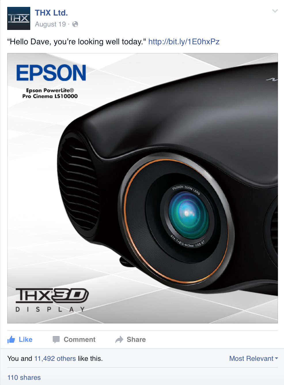 Close-up of an Epson PowerLite Pro Cinema LS10000 projector with a black matte finish and prominent lens, set against a light geometric background.