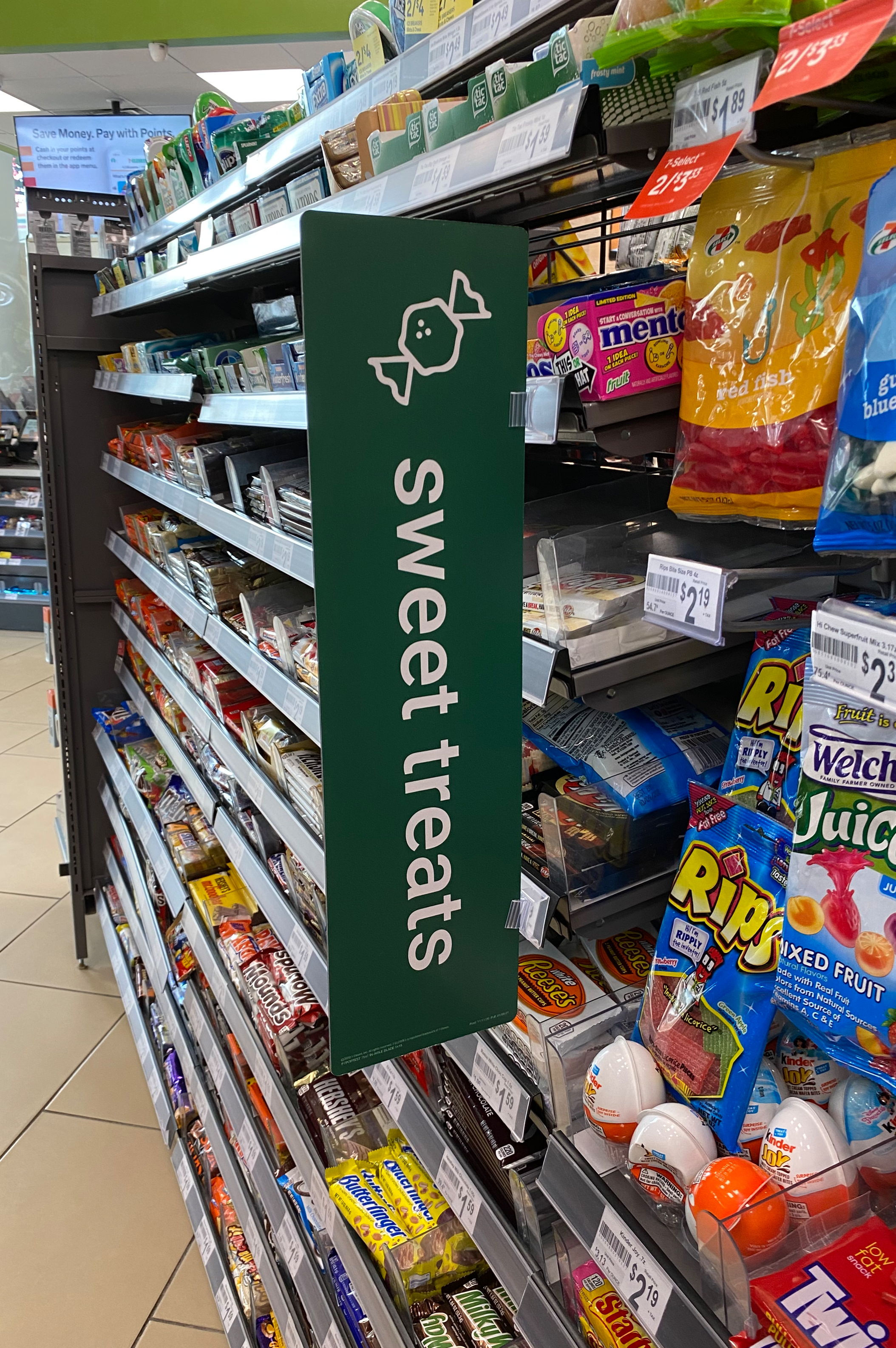 Shelf displaying assorted sweet treats with a green sign reading 'Sweet treats' and a graphic of a candy.