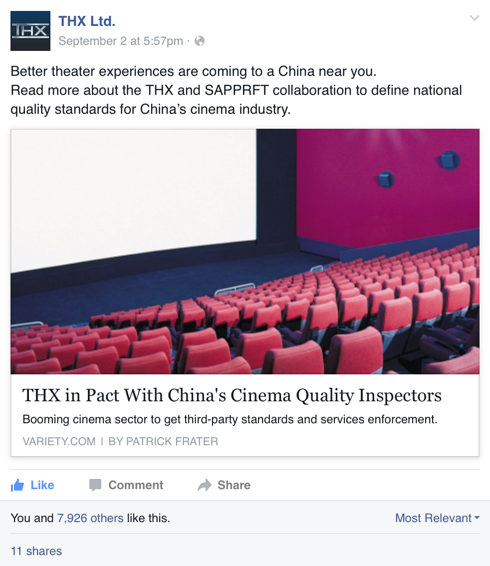 Image of a movie theater with red chairs and a large blank white screen, inside a dimly lit room. The theater has a pink wall with mounted speakers.