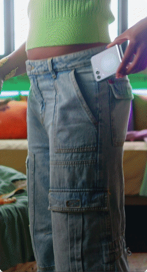 Person in a green top and cargo shorts holding a smartphone near their waistband.