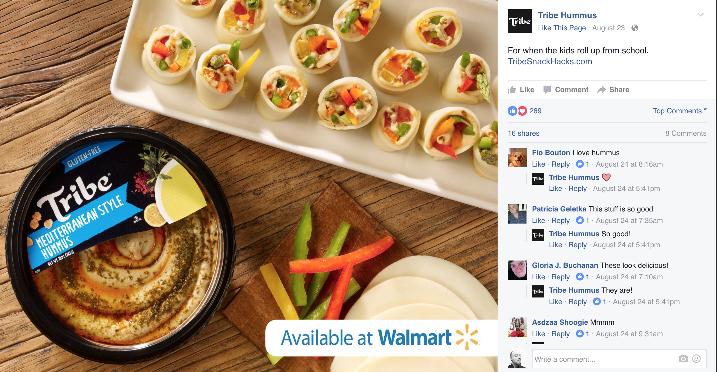 A tray of stuffed hard-boiled eggs filled with colorful vegetables, a container of Tribe hummus, and sliced vegetables on a wooden surface, with an advertisement indicating the hummus is available at Walmart.