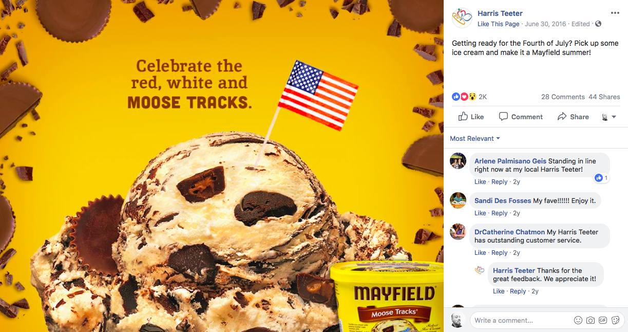 A container of Mayfield Moose Tracks ice cream with a scoop topped with chocolate chunks, some scattered on the yellow background. An American flag on a stick is inserted into the ice cream, with a message encouraging celebrating the Fourth of July with ice cream.