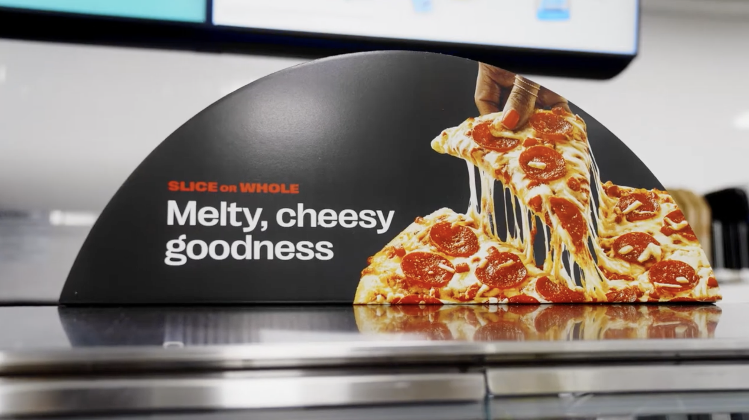 A pizza display sign showing a slice of pepperoni pizza with melted cheese being lifted, with the text 'SLICE on WHOLE Melty, cheesy goodness' written beside it.