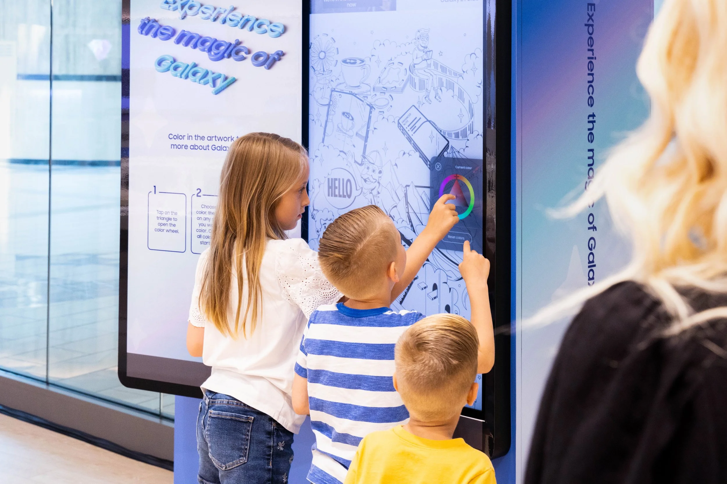 Children interacting with a digital art activity at a Galaxy-themed display, involving color selection on a touchscreen.