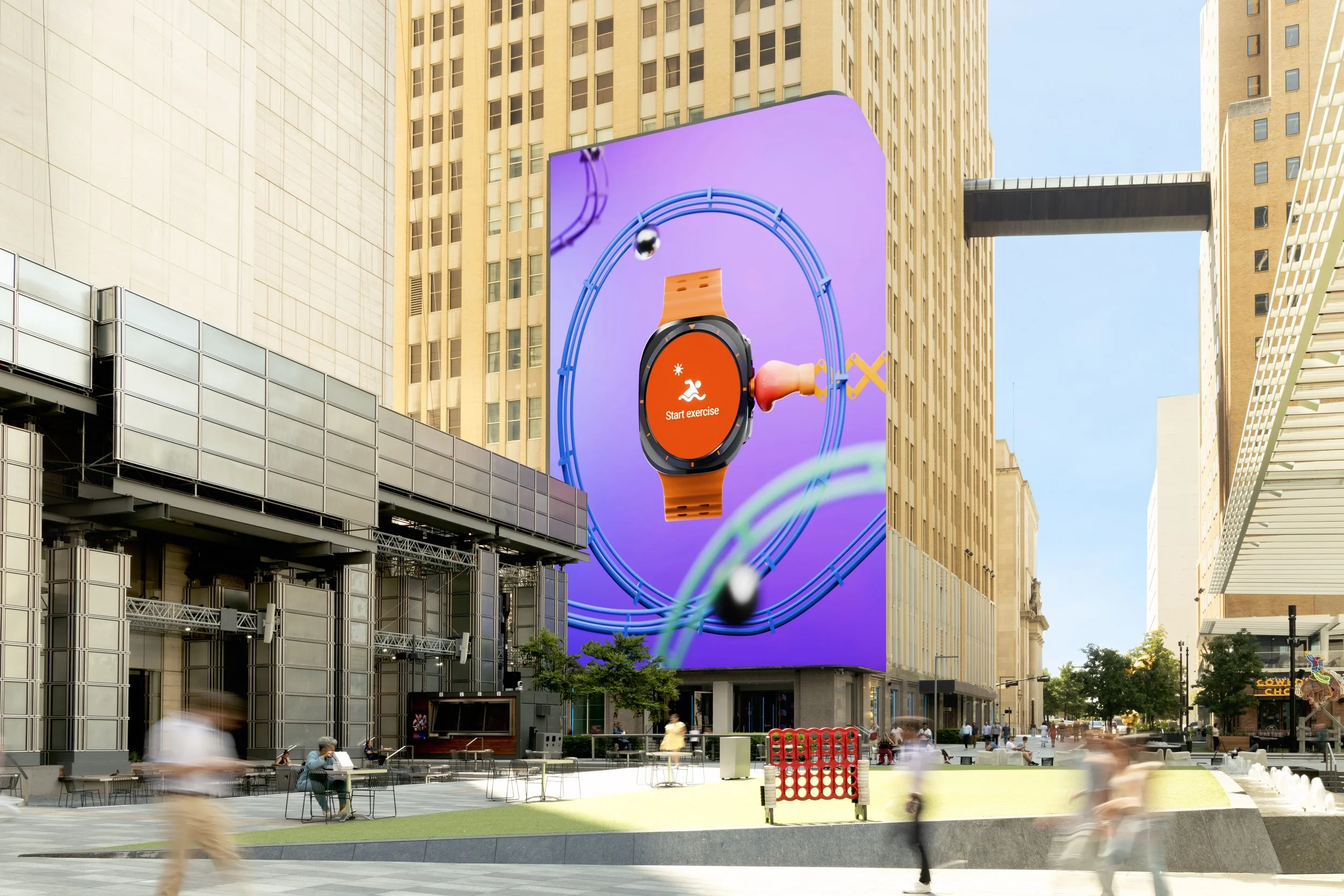 Large digital billboard in a city street displays a smartwatch interface with an orange band and a red screen showing an exercise start button. Surrounding the billboard are tall buildings and people walking in the area.