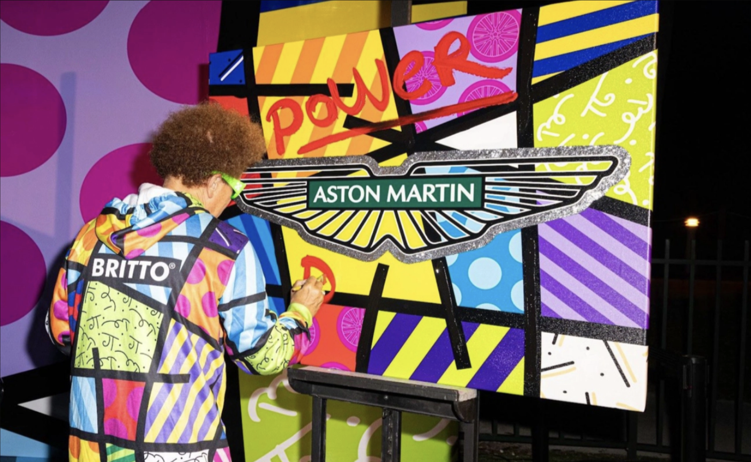 Person in colorful clothing drawing on a large, brightly decorated panel with a Chelsea Boot logo and the word 'POW' in red.