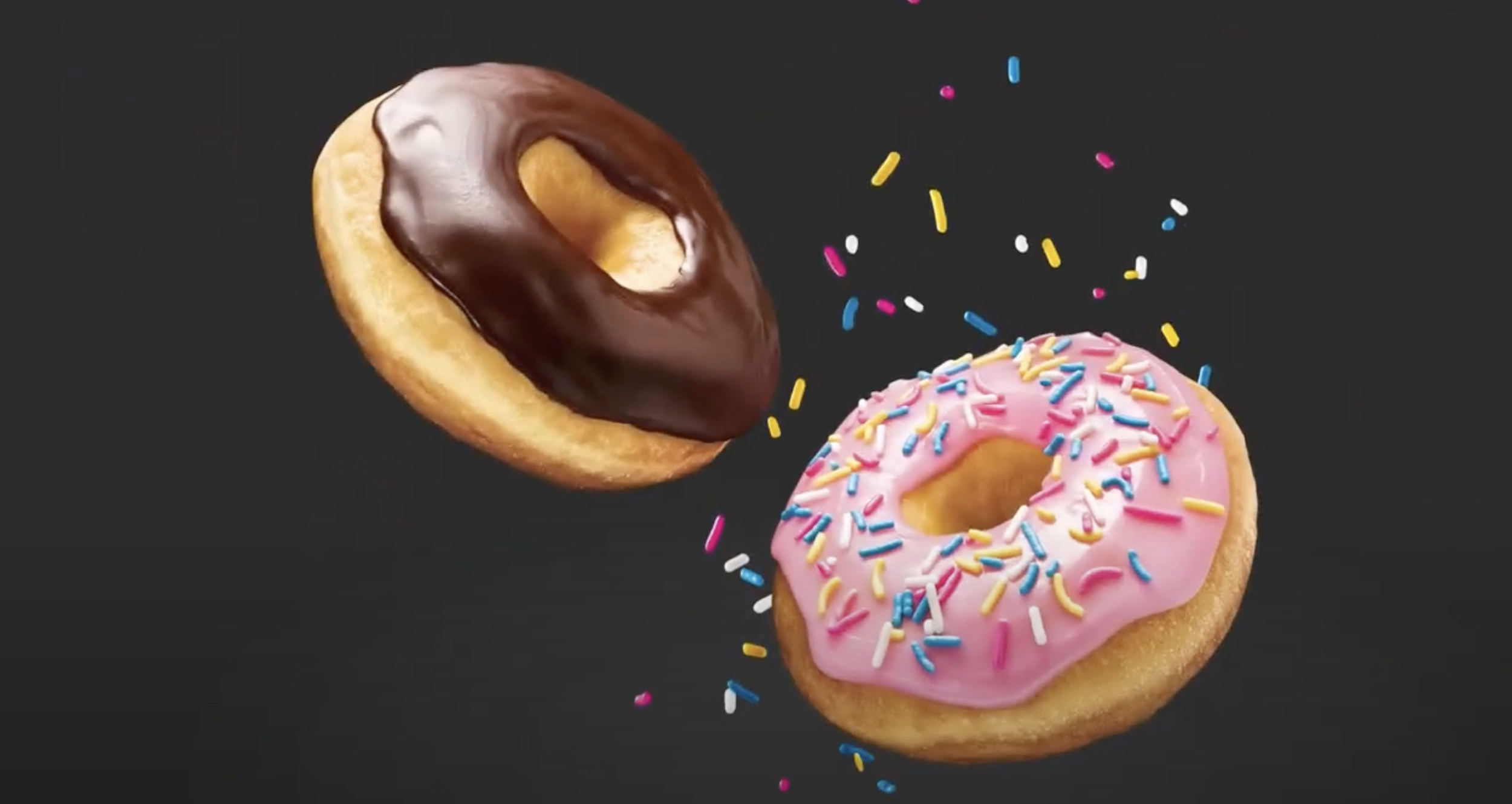 Two donuts, one with pink icing and multicolored sprinkles, the other with chocolate icing, are shown in mid-air against a black background.