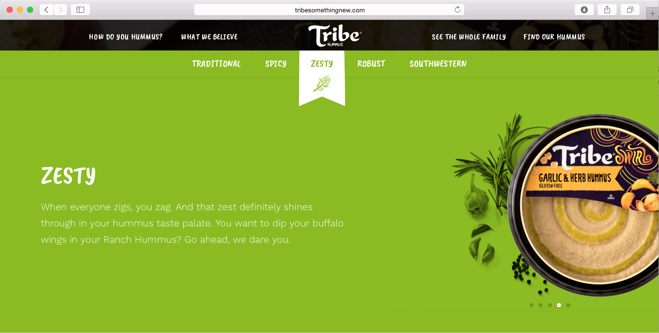 A webpage for Tribe Hummus featuring a close-up image of a container of garlic and herb hummus with a decorative label, along with fresh herbs and garlic on a bright green background.