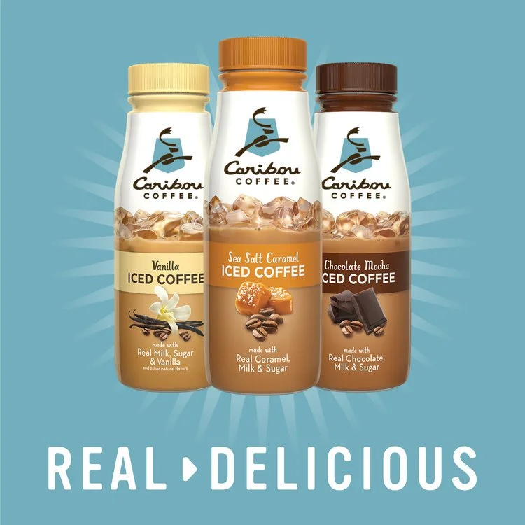 Three bottles of Caribou Coffee iced coffee drinks in vanilla, sea salt caramel, and chocolate mocha flavors, placed against a blue background with a radial burst design, with the words "REAL DELICIOUS" at the bottom.