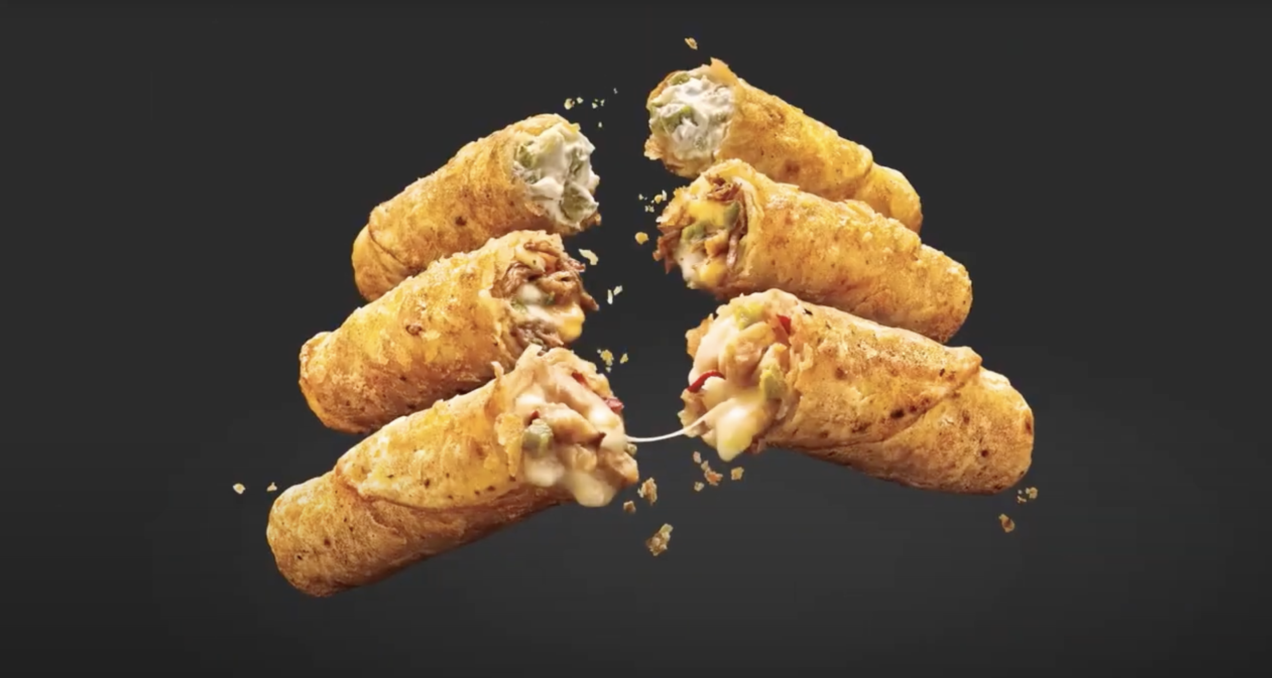 Six fried jalapeno poppers with creamy cheese filling on black background, some cheese melting and crumbs scattered.