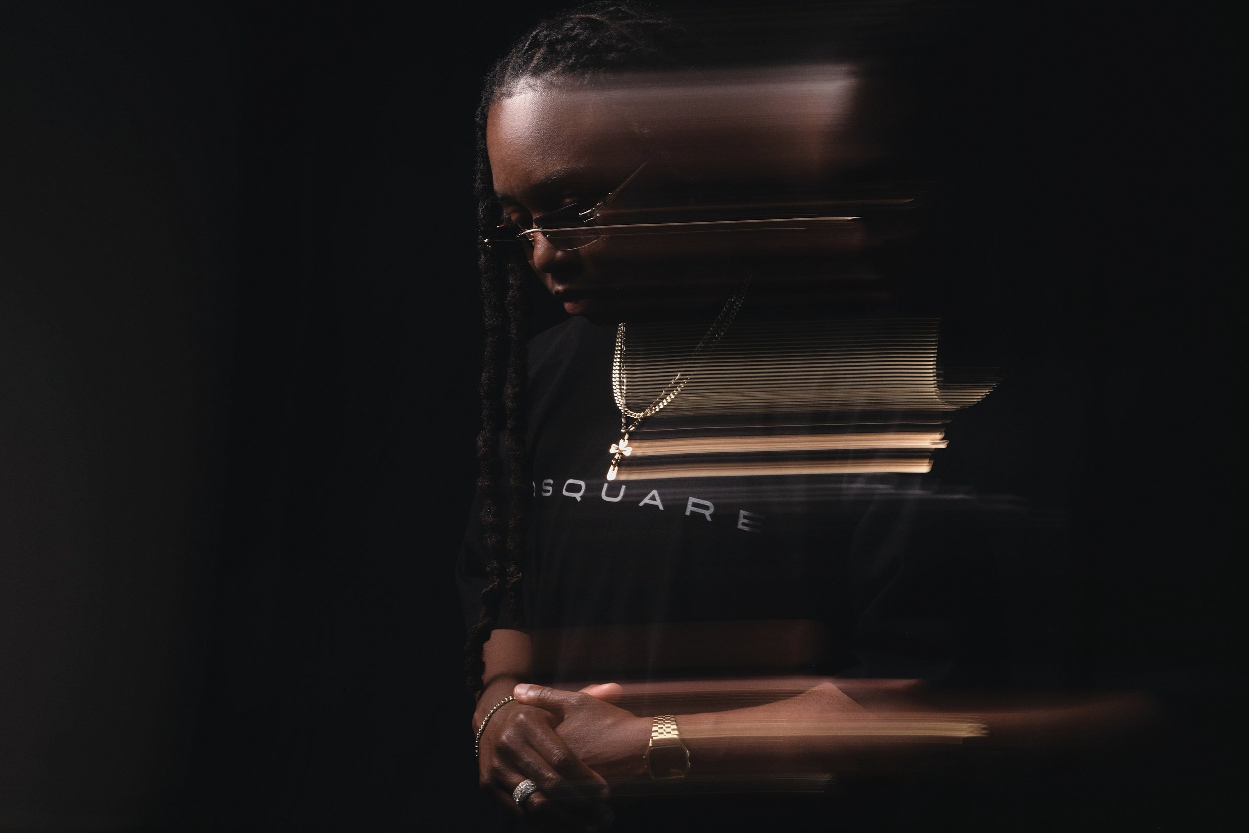Portrait of a Black artist wearing an OSQUARE shirt, captured with motion blur effects against a dark background.