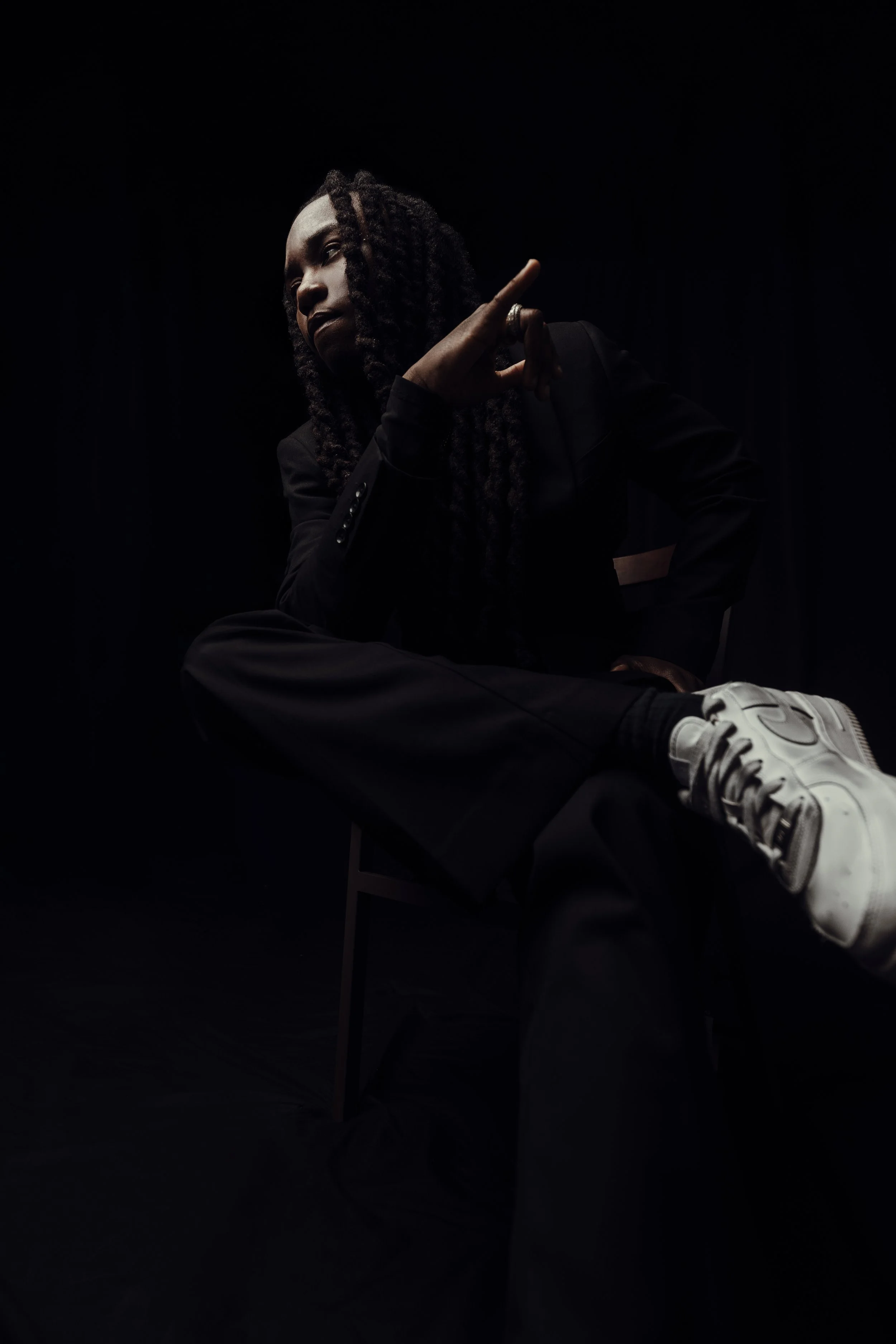OSQUARE, independent alternative R&B artist, seated in a black suit against a dark studio backdrop.