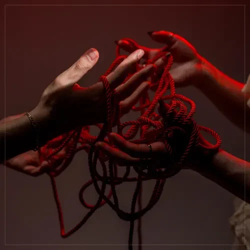 Two hands holding tangled red rope in a dark setting with a reddish hue.