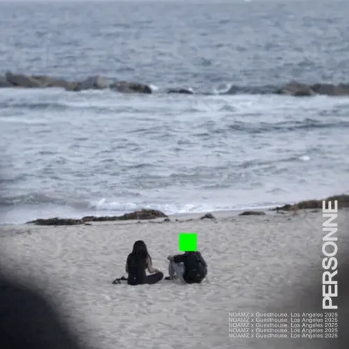 Two people sitting on a sandy beach near the water, facing the ocean.
