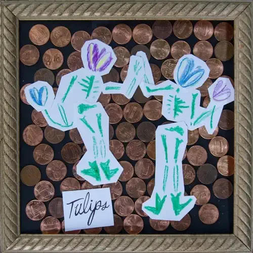 Artwork labeled "Tulips" featuring paper cutouts of three stylized tulip flowers with green stems and purple, blue, and violet petals, placed on a background of scattered pennies in a wooden frame.