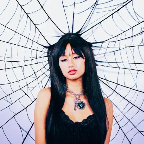 Young woman with long black hair and dark makeup in front of a spider web backdrop.