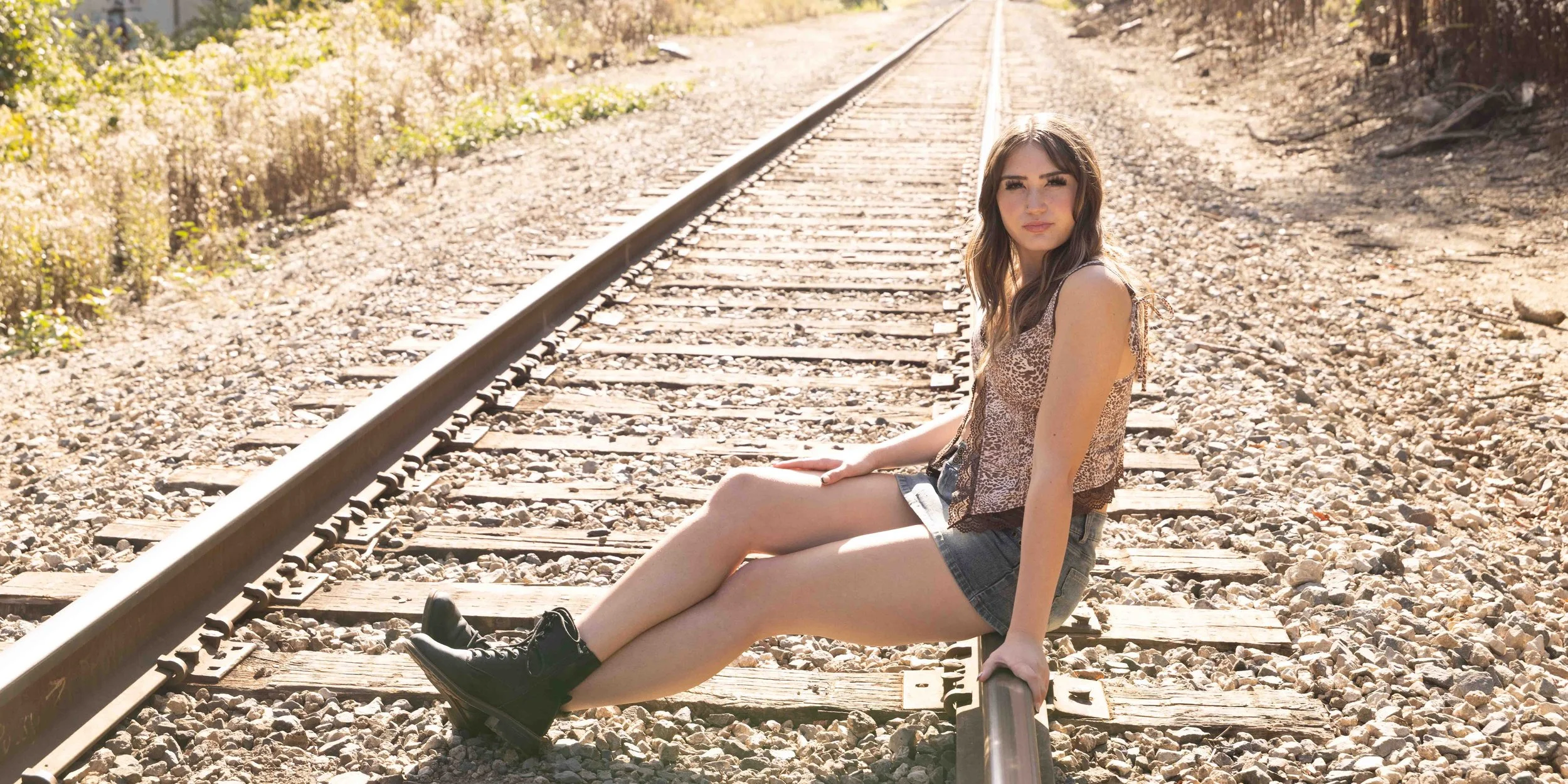 Young woman sitting on railroad track during daytime in a rural area.