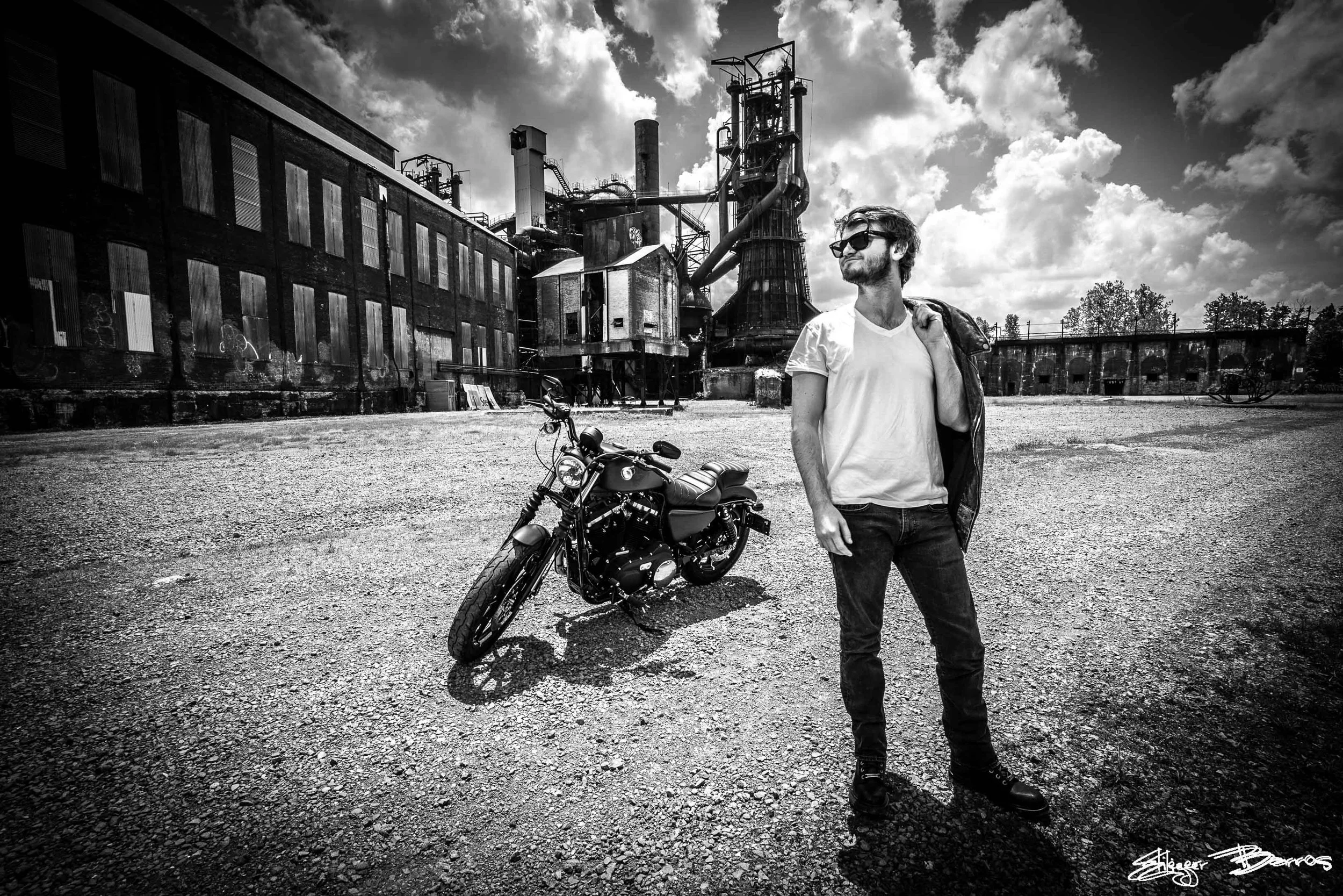 Senior Pictures Pittsburgh at Carrie Furnace. Young man with beard and sunglasses standing next to a motorcycle in front of historic industrial blast furnaces for bold black and white urban senior portraits.