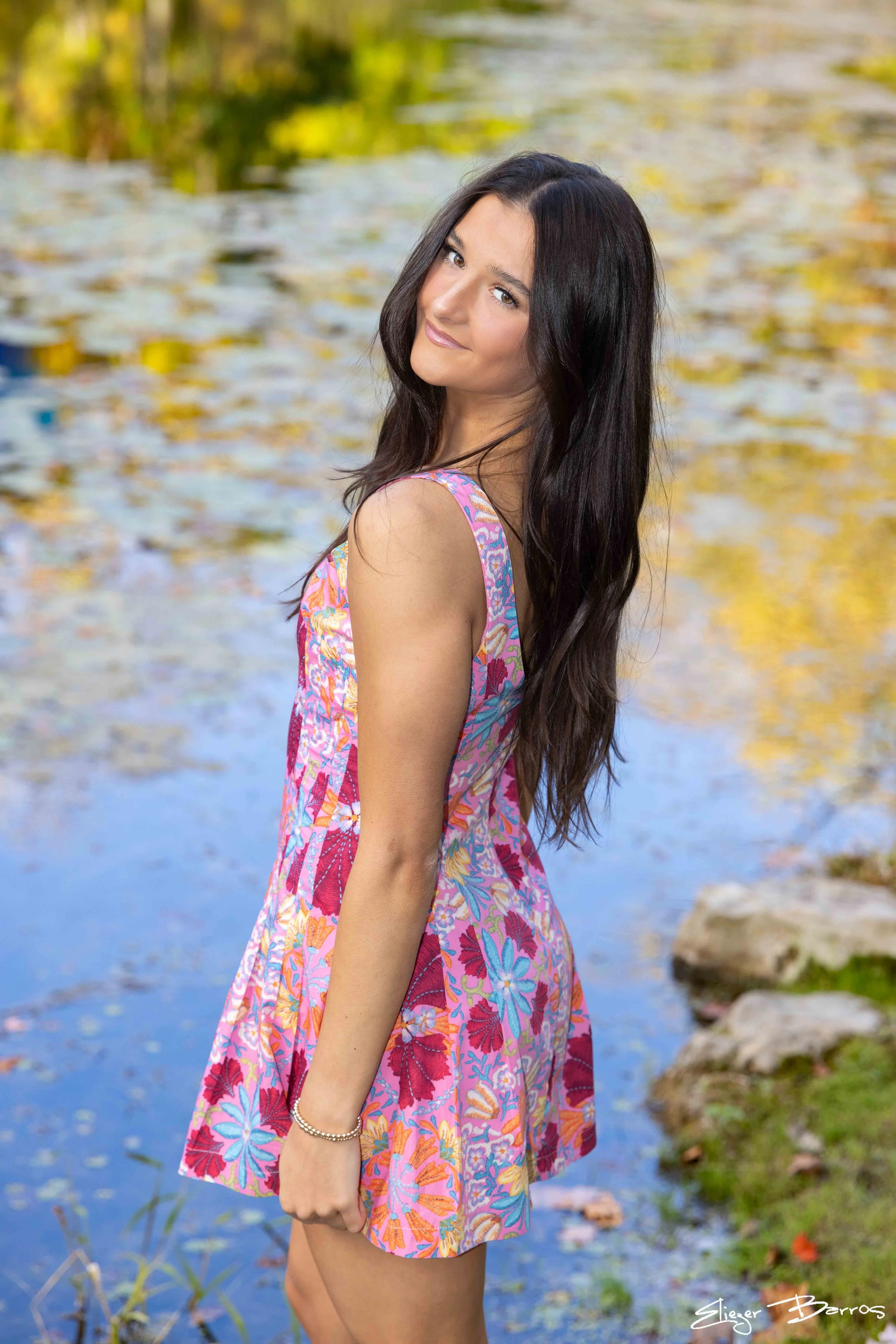 Class of 2026 senior Gianna in a colorful dress posing by the water at Pittsburgh Botanic Garden during her fall senior session