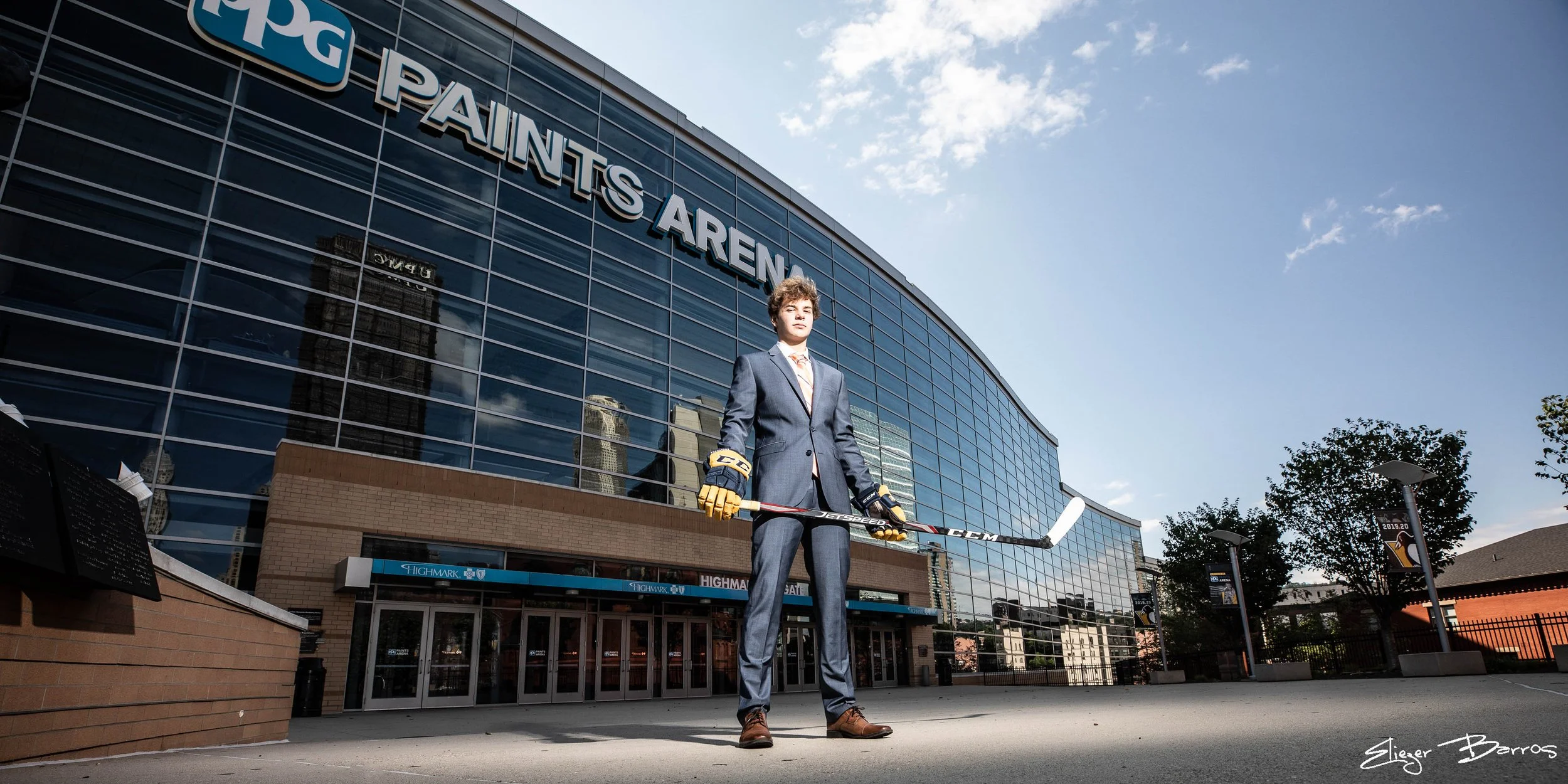 Senior Pictures Pittsburgh at PPG Paints Arena. Young man in a suit holding a hockey stick posing in front of the iconic arena during his downtown outdoor senior photoshoot.