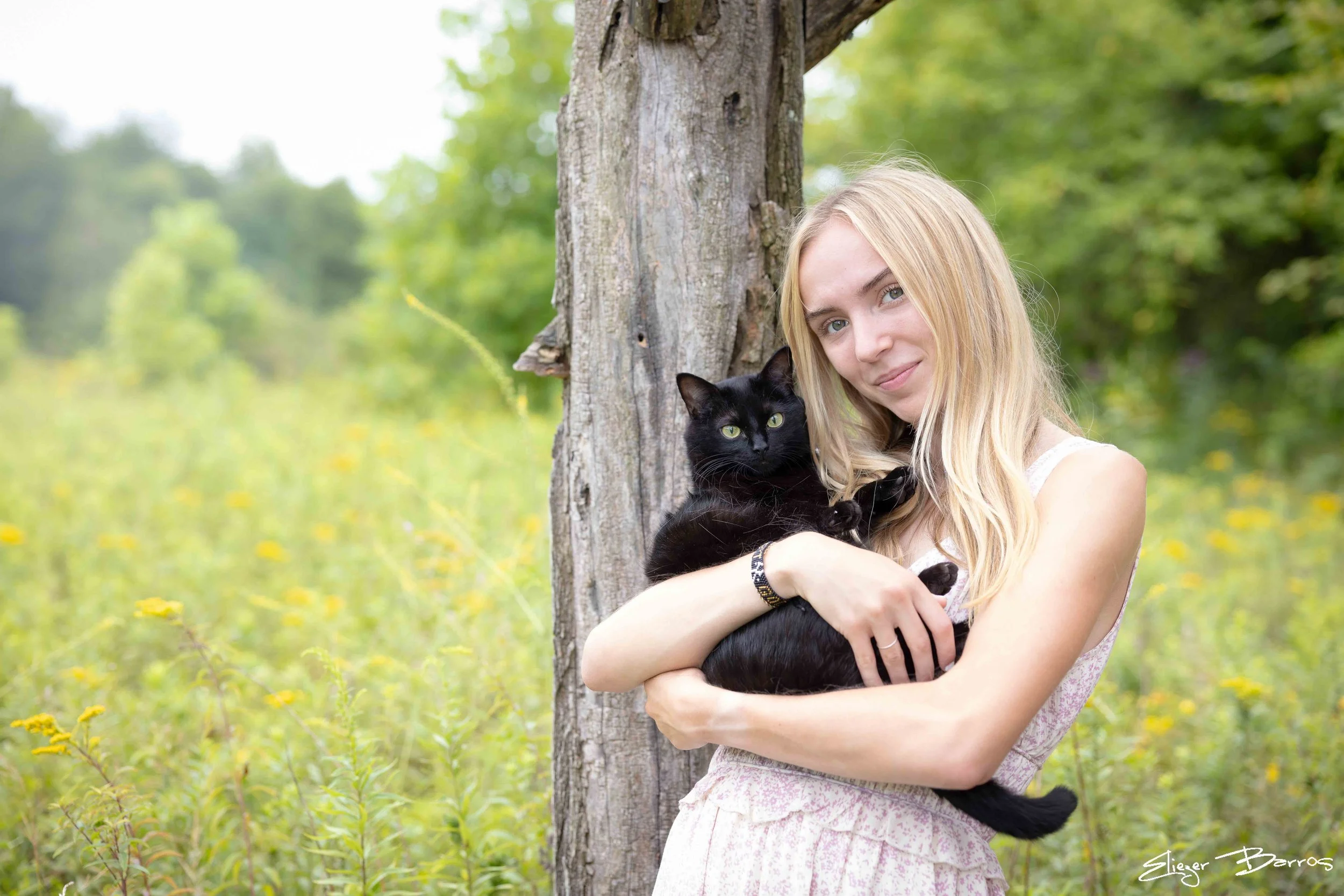Senior Pictures Pittsburgh at Pittsburgh Botanic Garden. Blonde senior girl holding a black cat while leaning against a tree during her natural outdoor senior photoshoot.