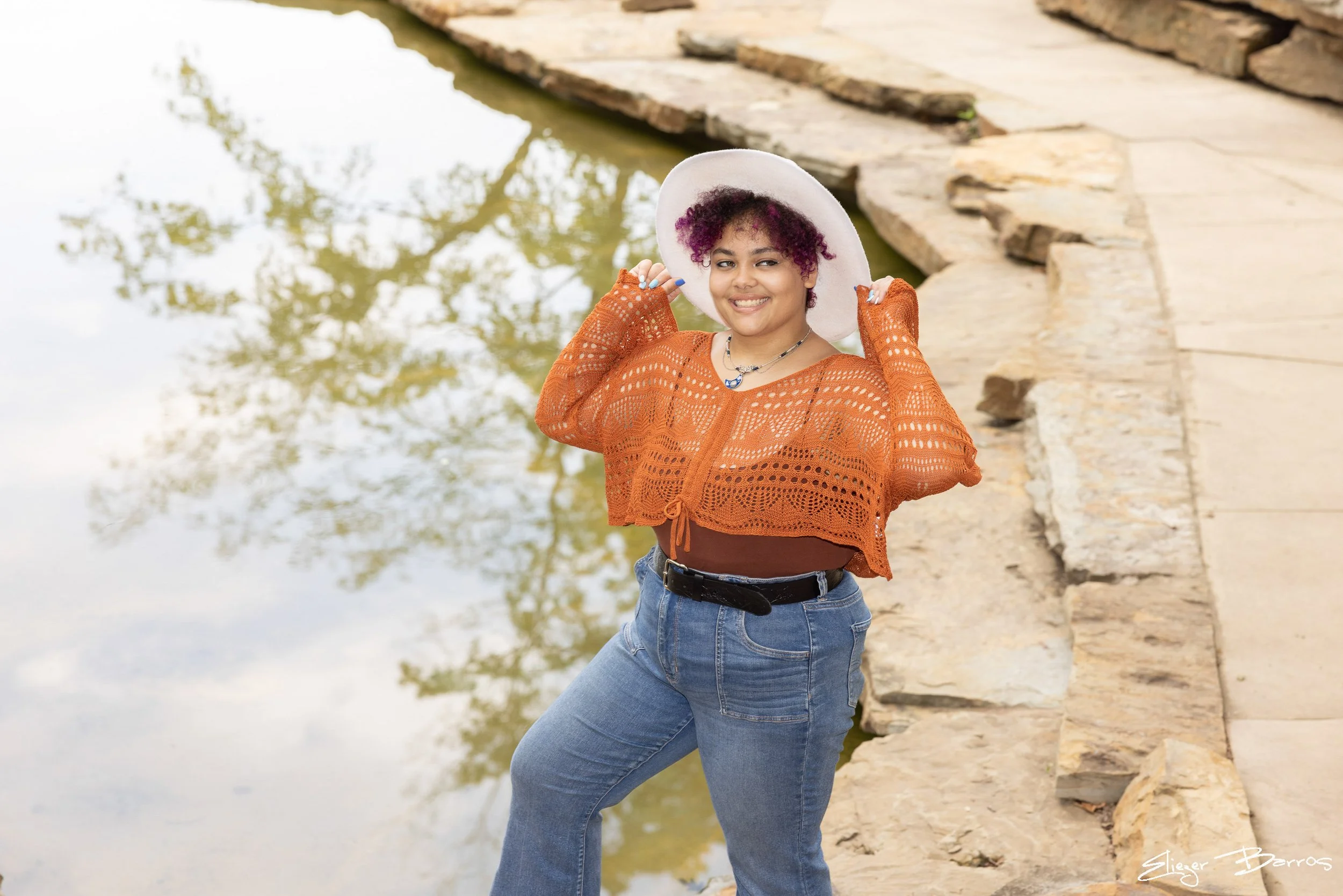 Senior Pictures Pittsburgh at The Cascades South Park. Young woman with purple hair in an orange sweater posing on stone steps by the waterfall at Oliver Miller Homestead for unique outdoor senior pictures.