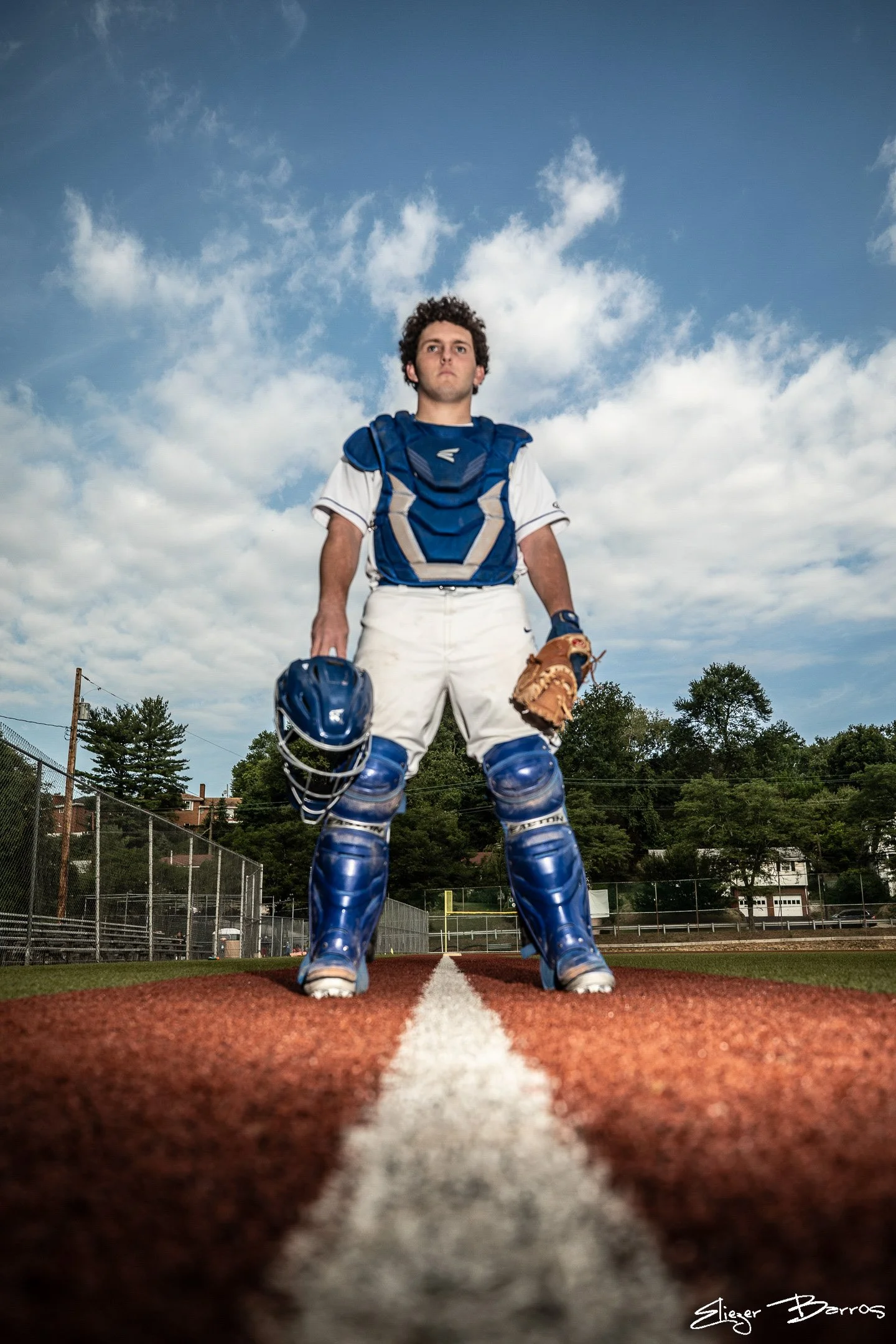 Senior Pictures Pittsburgh high school sports. Young man in full baseball catcher gear posing on the field with sky and trees behind him for classic athlete senior pictures.