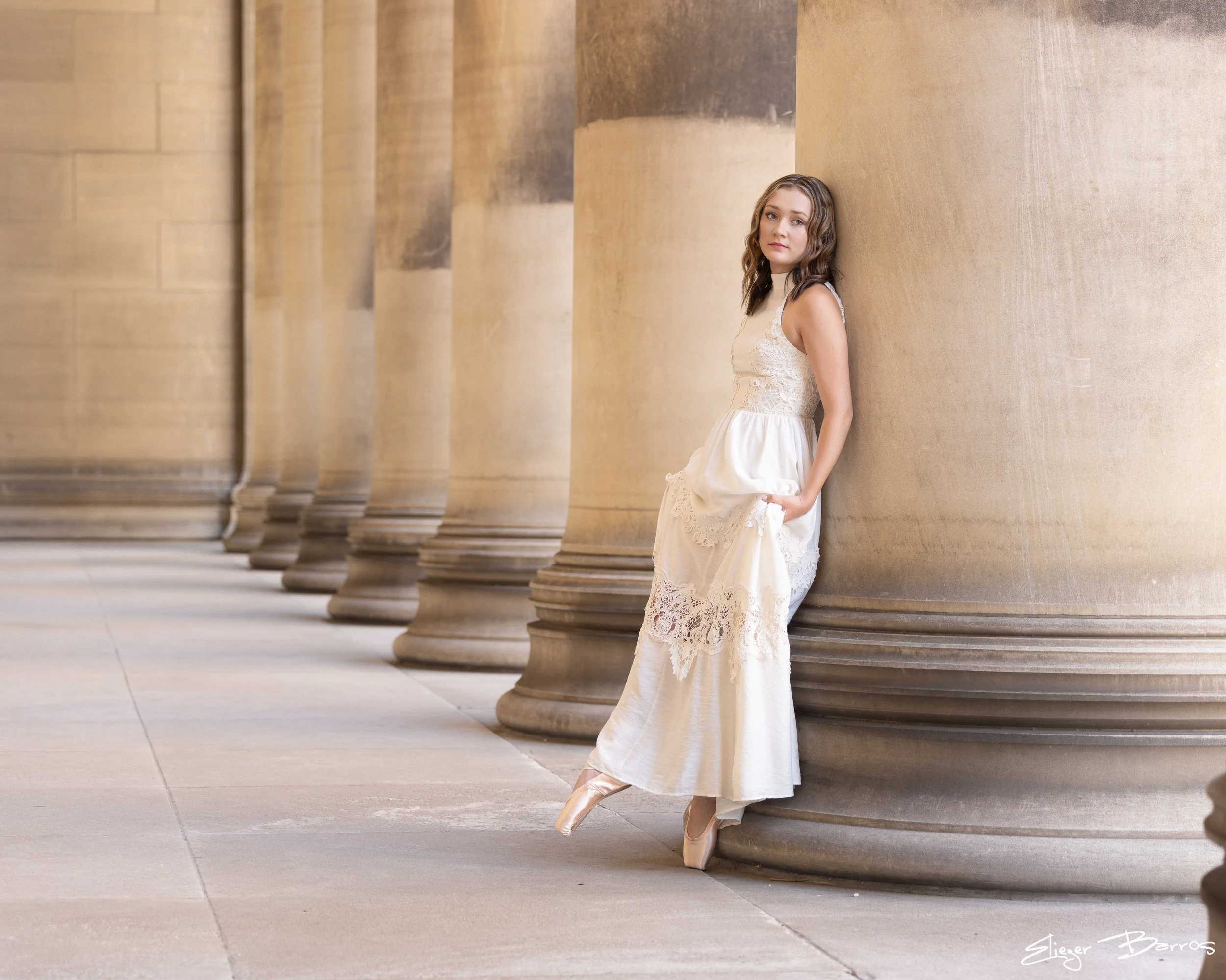 Senior Pictures Pittsburgh in Oakland. Young woman in a white dress leaning against large classical columns at Heinz Chapel or Mellon Institute for timeless outdoor senior pictures.