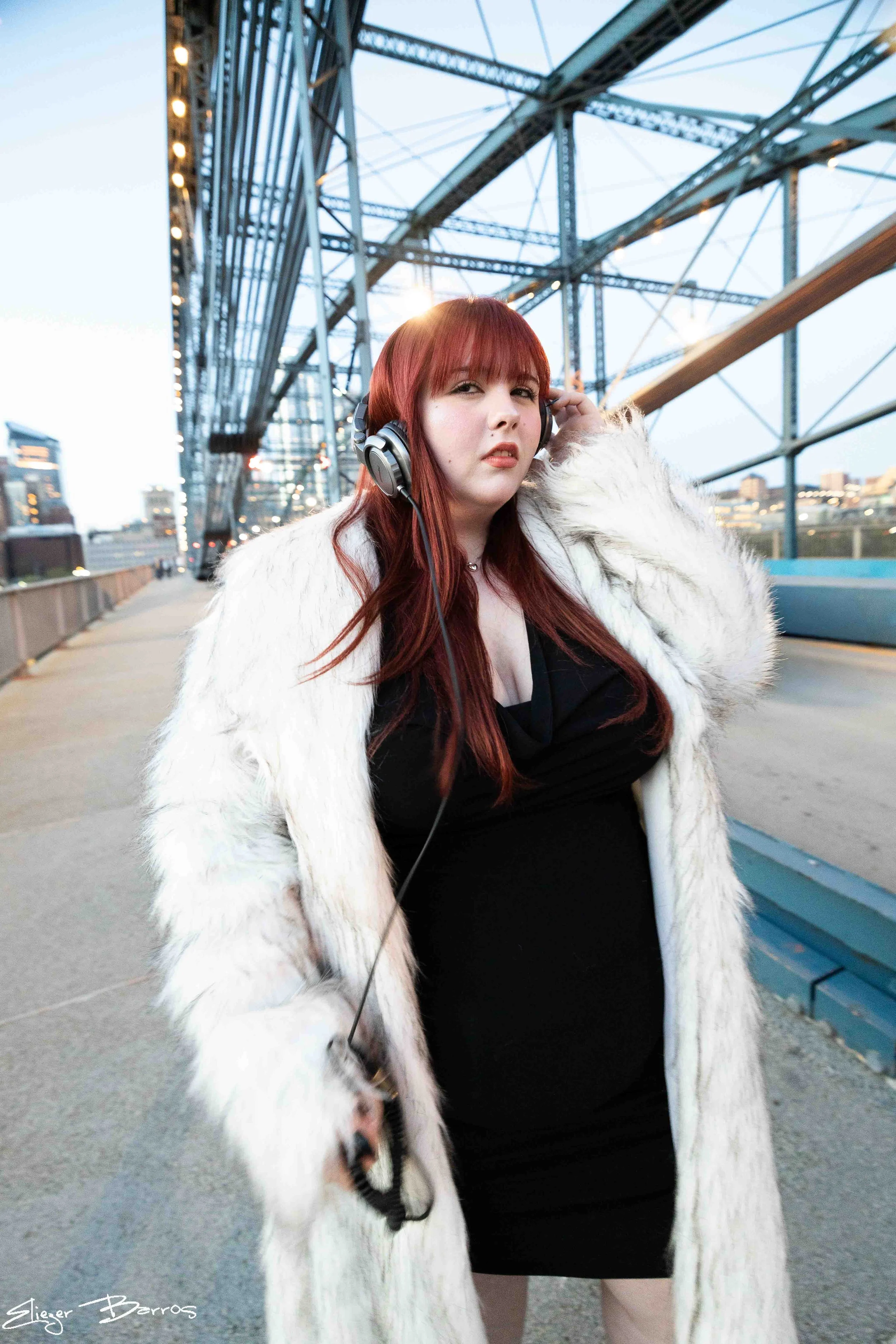 Class of 2026 senior Sydney posing confidently on the bridge at Station Square Pittsburgh wearing white fur coat and headphones