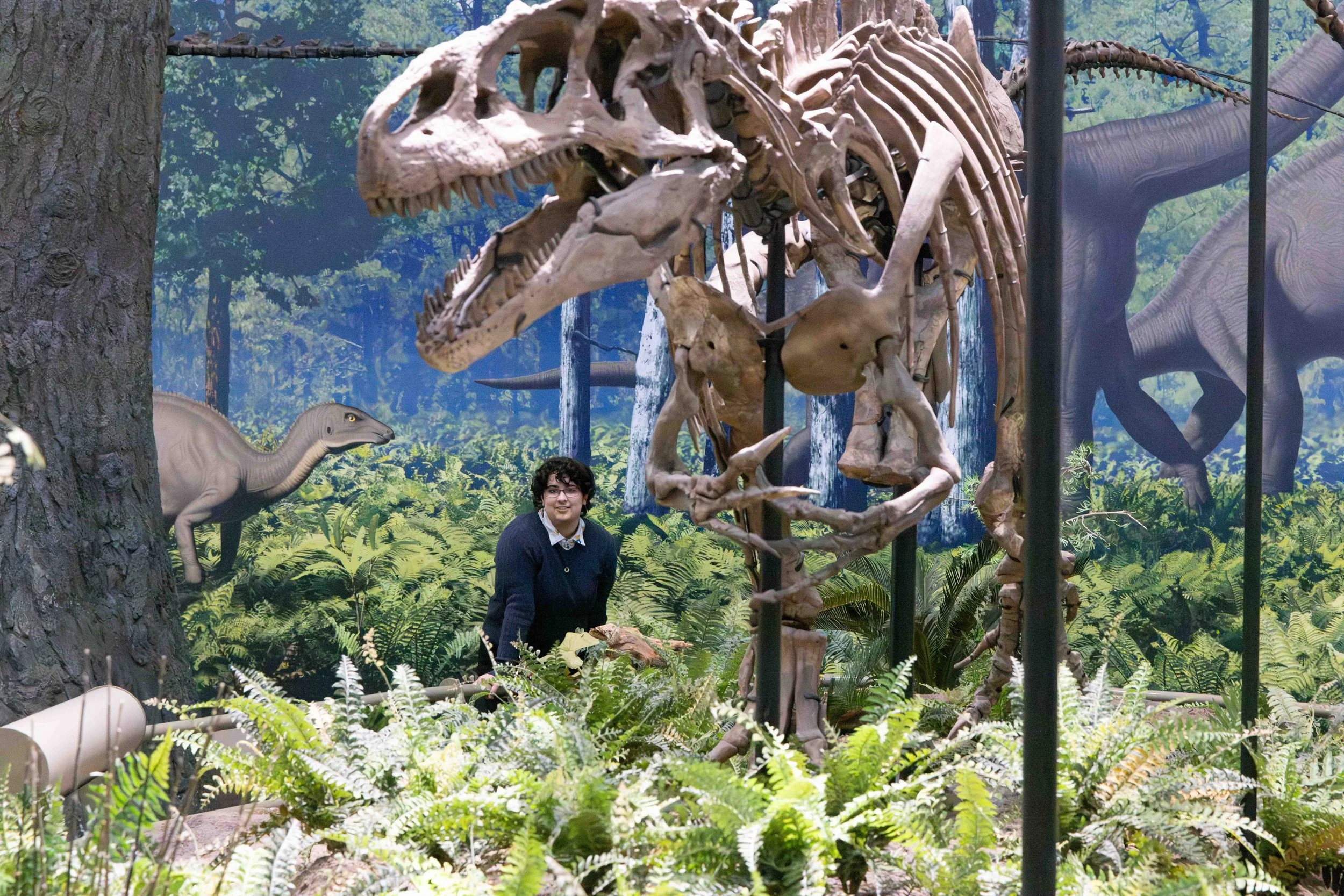 Class of 2027 senior Shanti posing in front of the dinosaur exhibit at Carnegie Museum of Natural History Pittsburgh