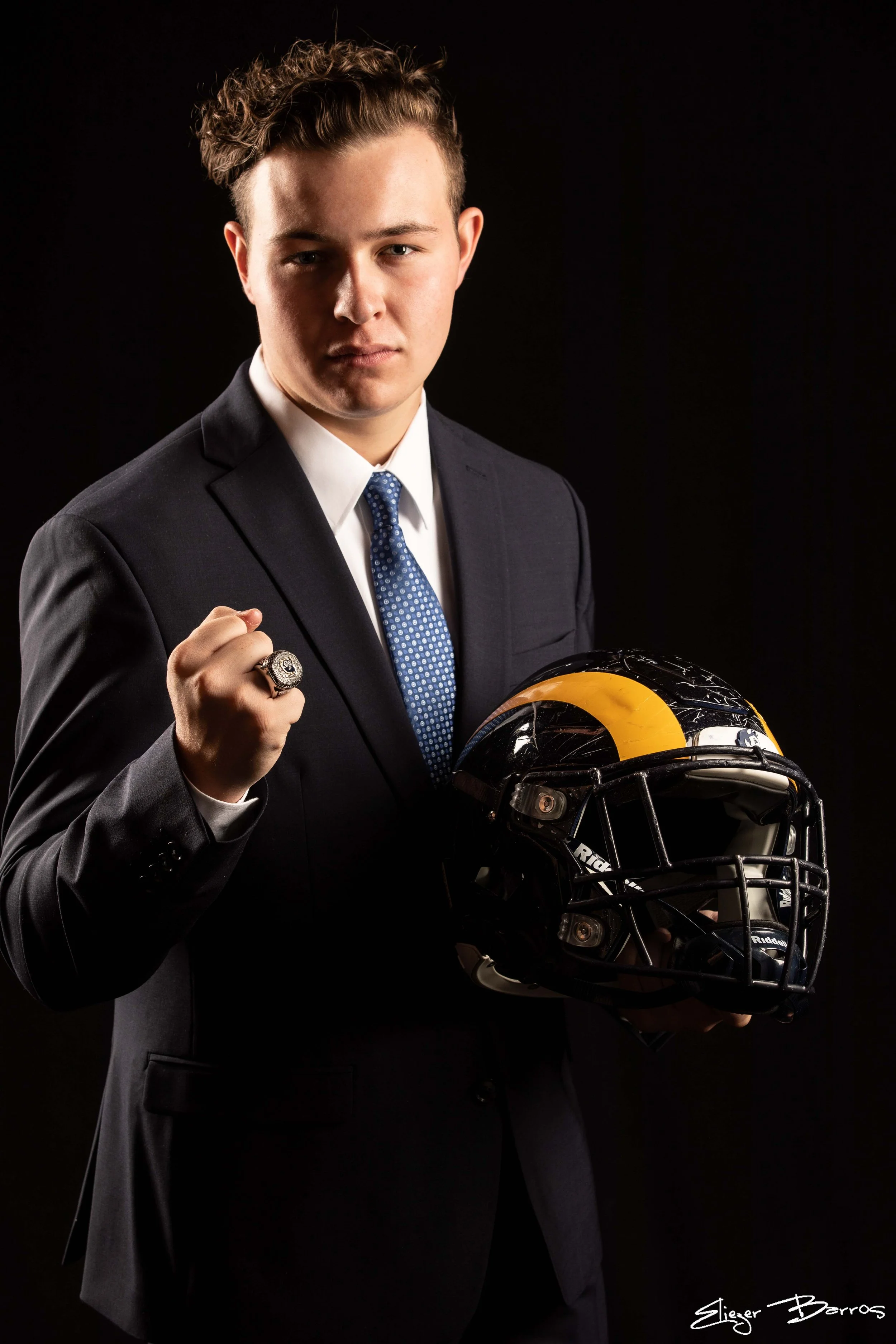 Senior pictures of a young man in suit holding football helmet in Pittsburgh studio