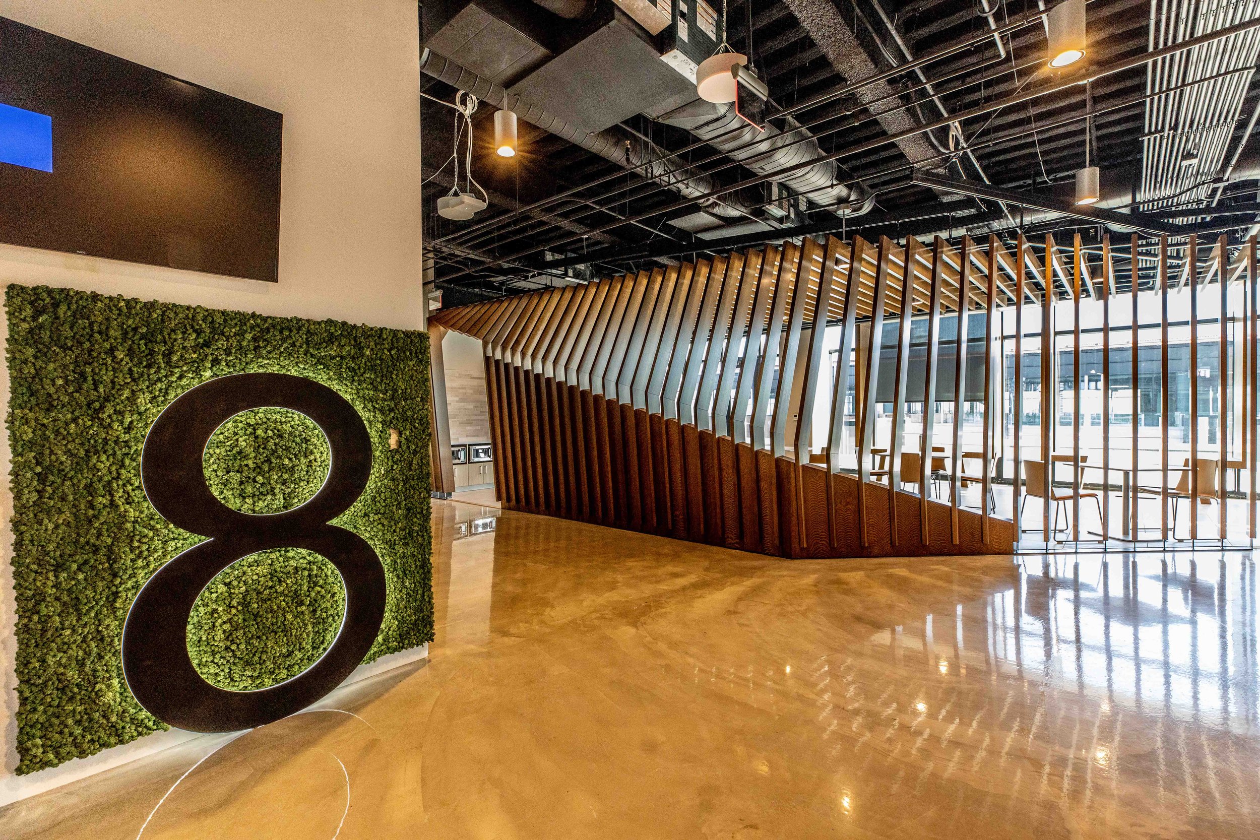 Modern indoor space with wooden slatted divider, green moss wall with large black number 8, ceiling with exposed ductwork, and a marble floor.
