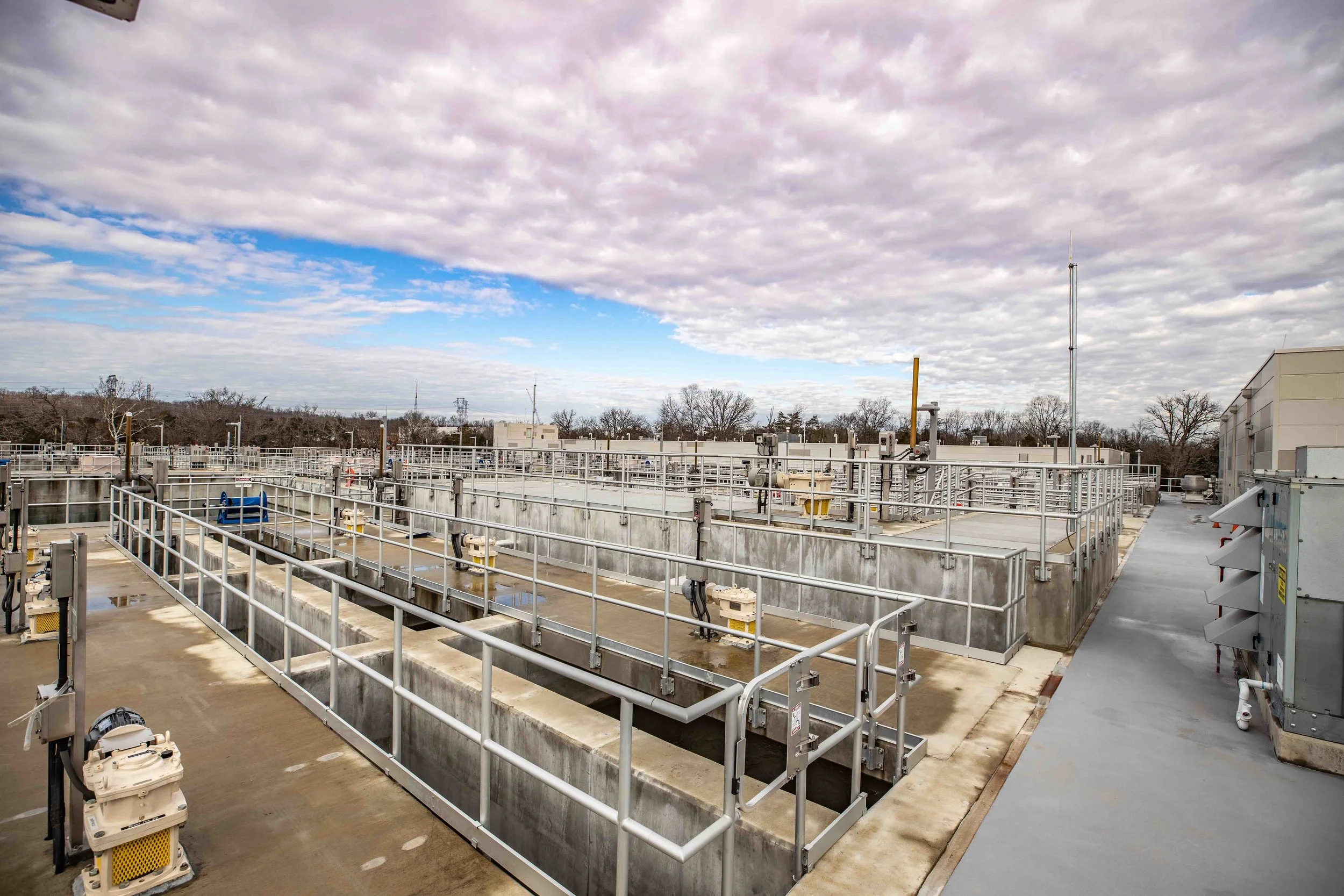 A view of a water treatment plant with several basins and machinery, under a partly cloudy sky.