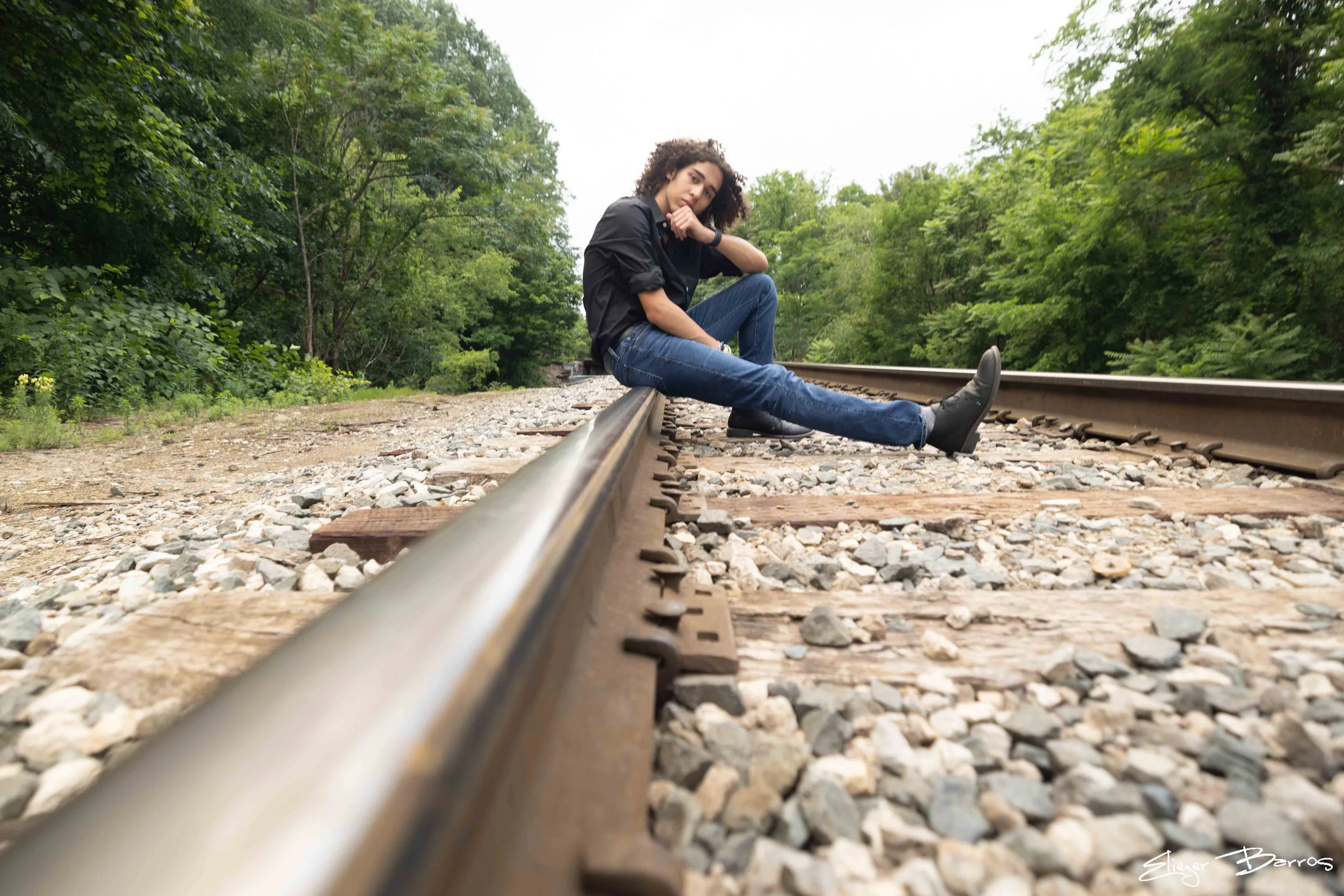 A woman sitting on a railroad track surrounded by green trees.