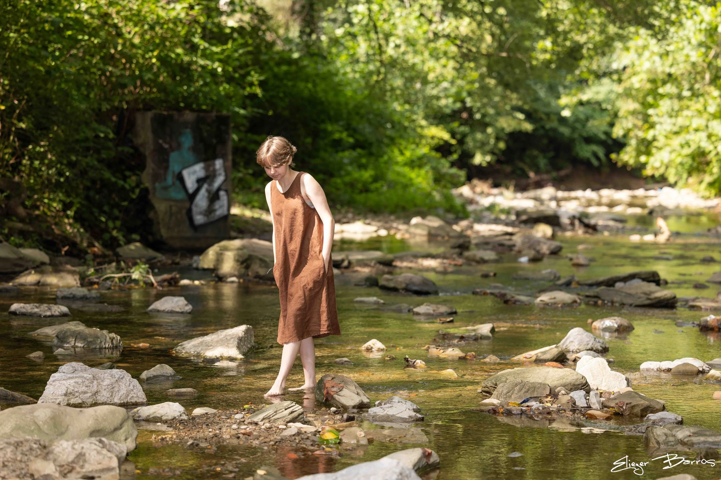 Senior Pictures Pittsburgh at Seldom Seen Greenway. Young woman in a brown dress standing in a rocky creek surrounded by lush green woods for adventurous natural outdoor senior portraits.